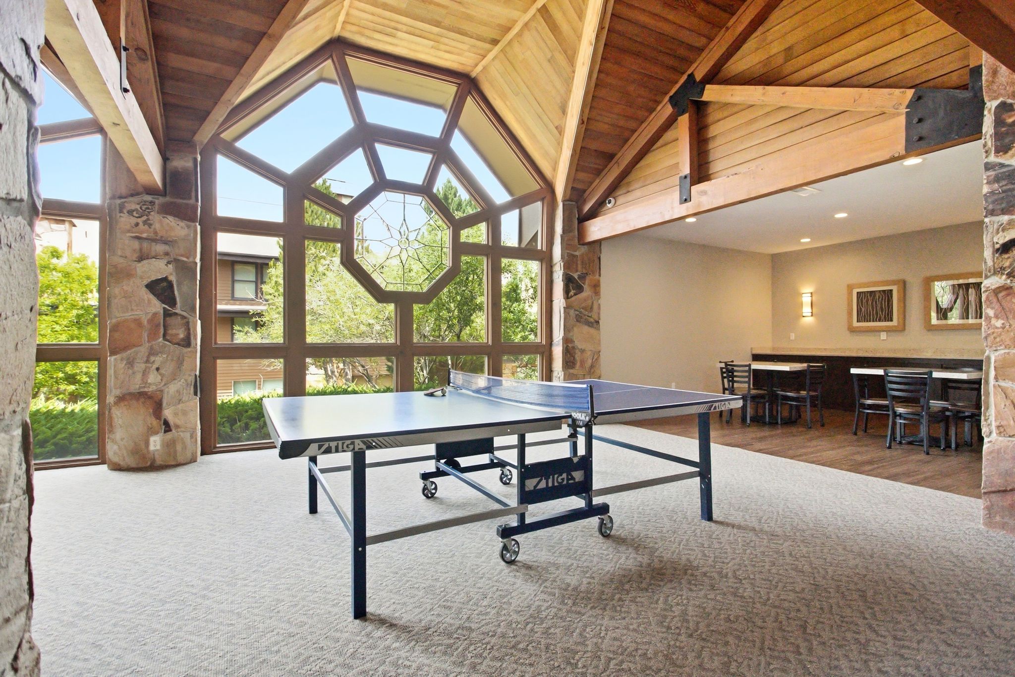 Expansive recreation room featuring a vaulted wood-beam ceiling, floor-to-ceiling geometric windows, and stone accents