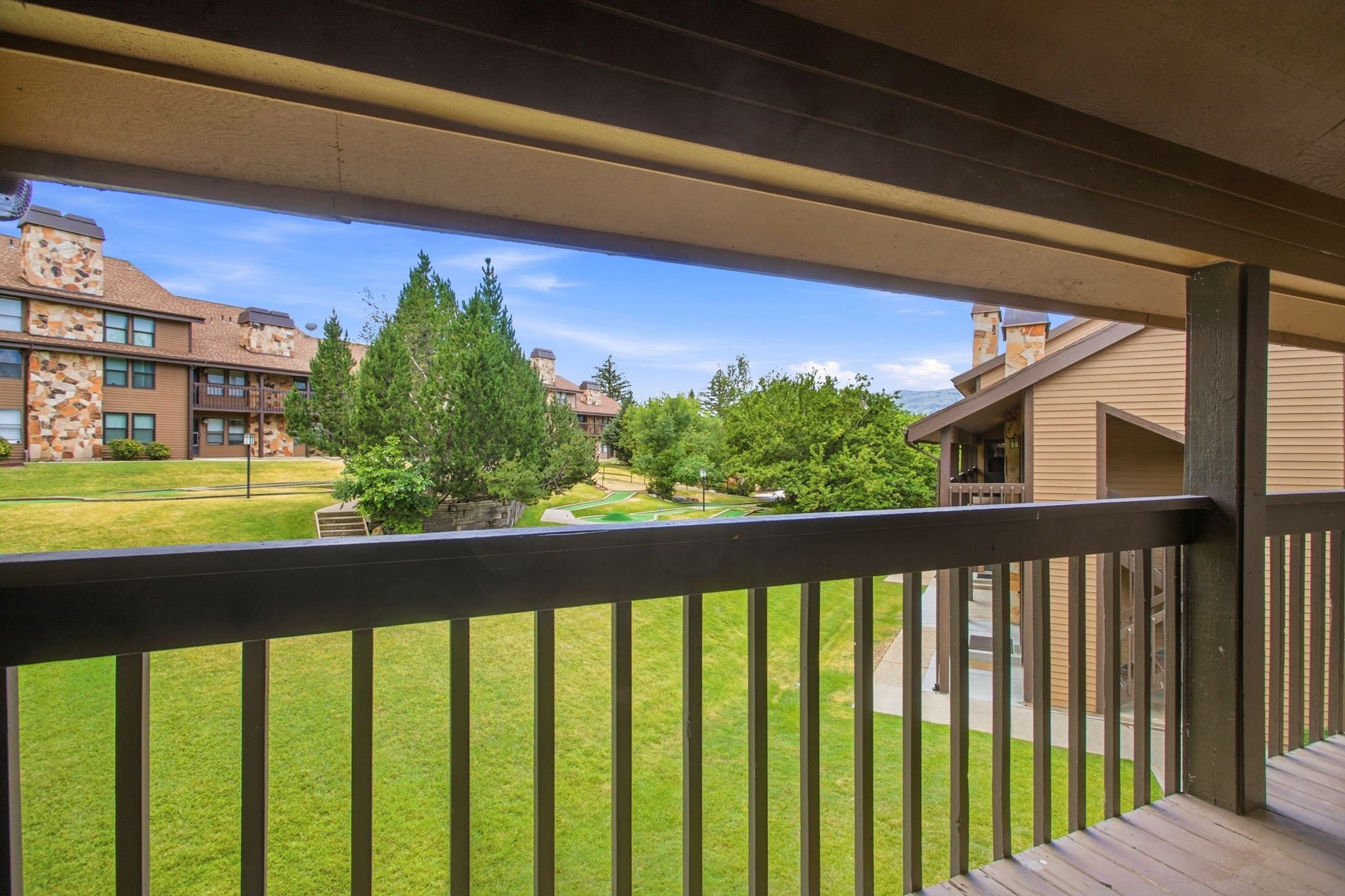 Wood-finish balcony with dark railings overlooking a manicured lawn area with mature trees