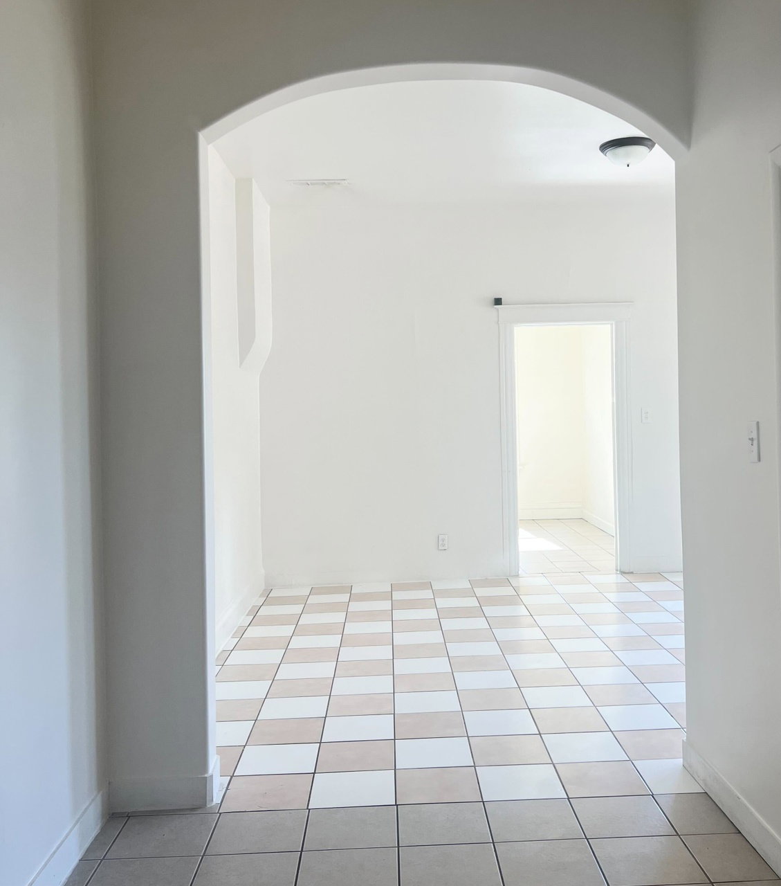 Arched entryway opening to a room featuring checkerboard tile flooring and a ceiling-mounted light fixture