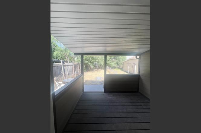 Covered outdoor patio featuring wood-finish flooring, a solid privacy wall, and a view of the backyard