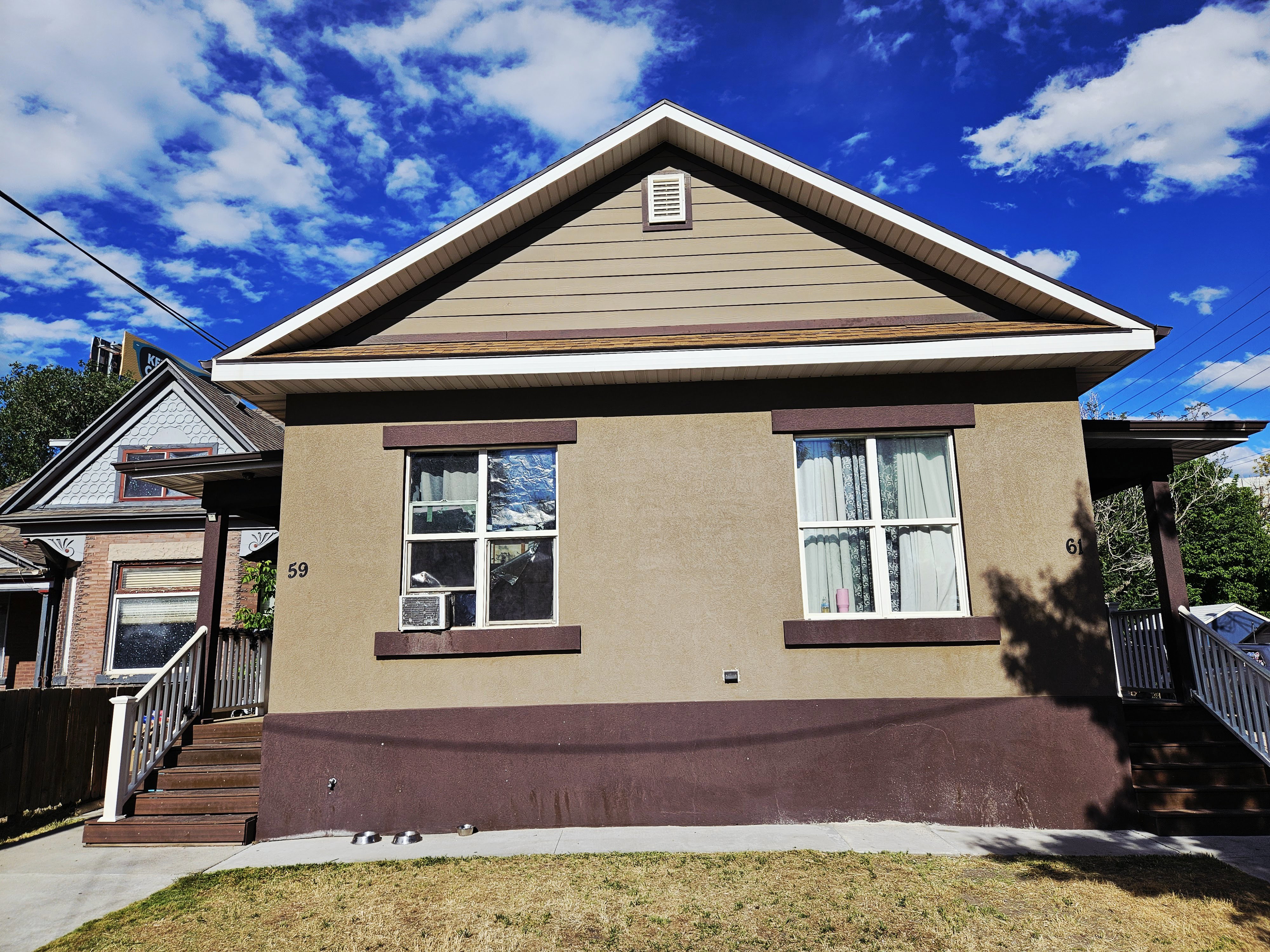 Exterior features include a gabled roofline with brown shingles, tan siding on the gable, and a tan stucco facade with brown trim