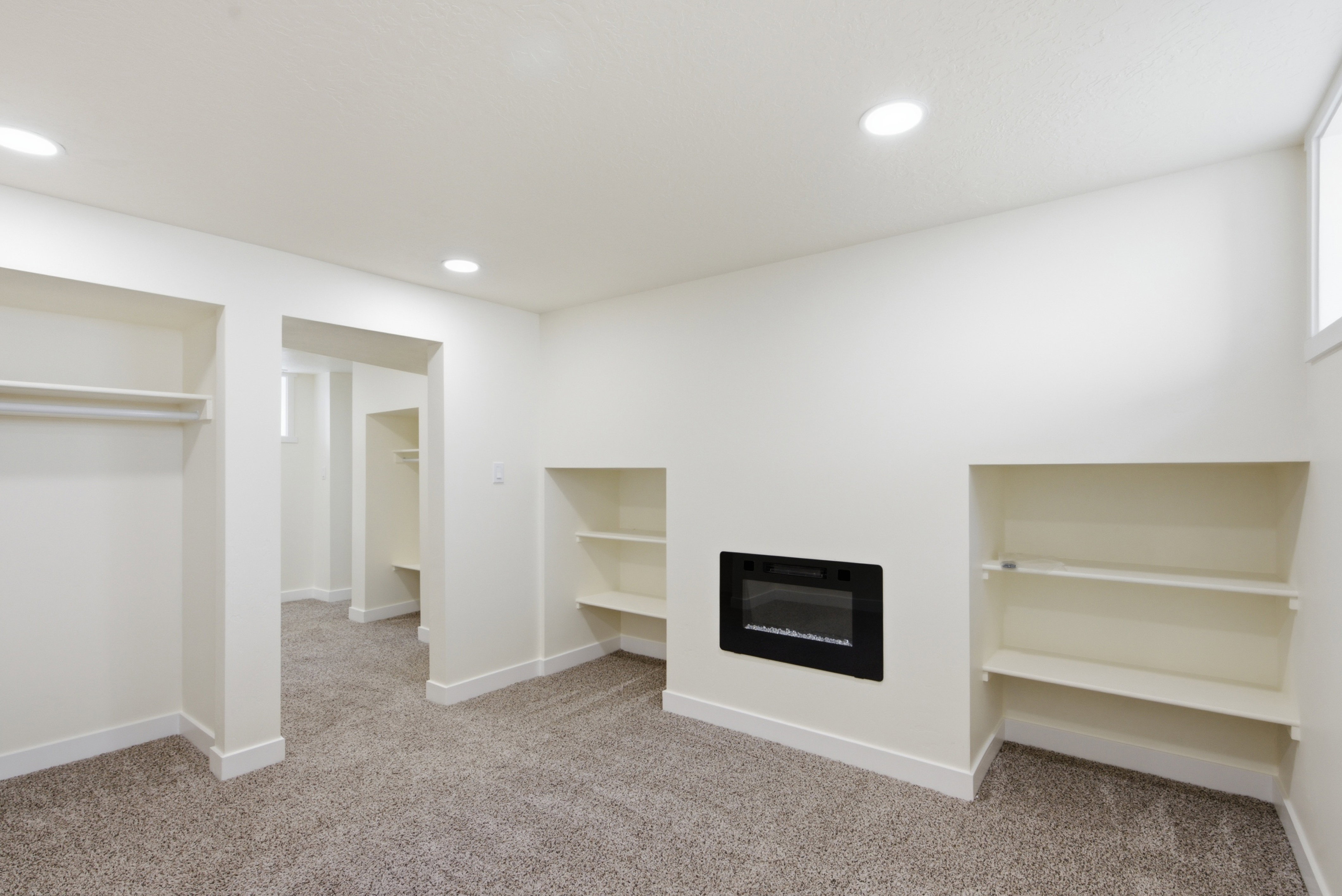 Recessed electric fireplace with built-in shelving, plush carpet flooring, recessed lighting, and a window for natural illumination