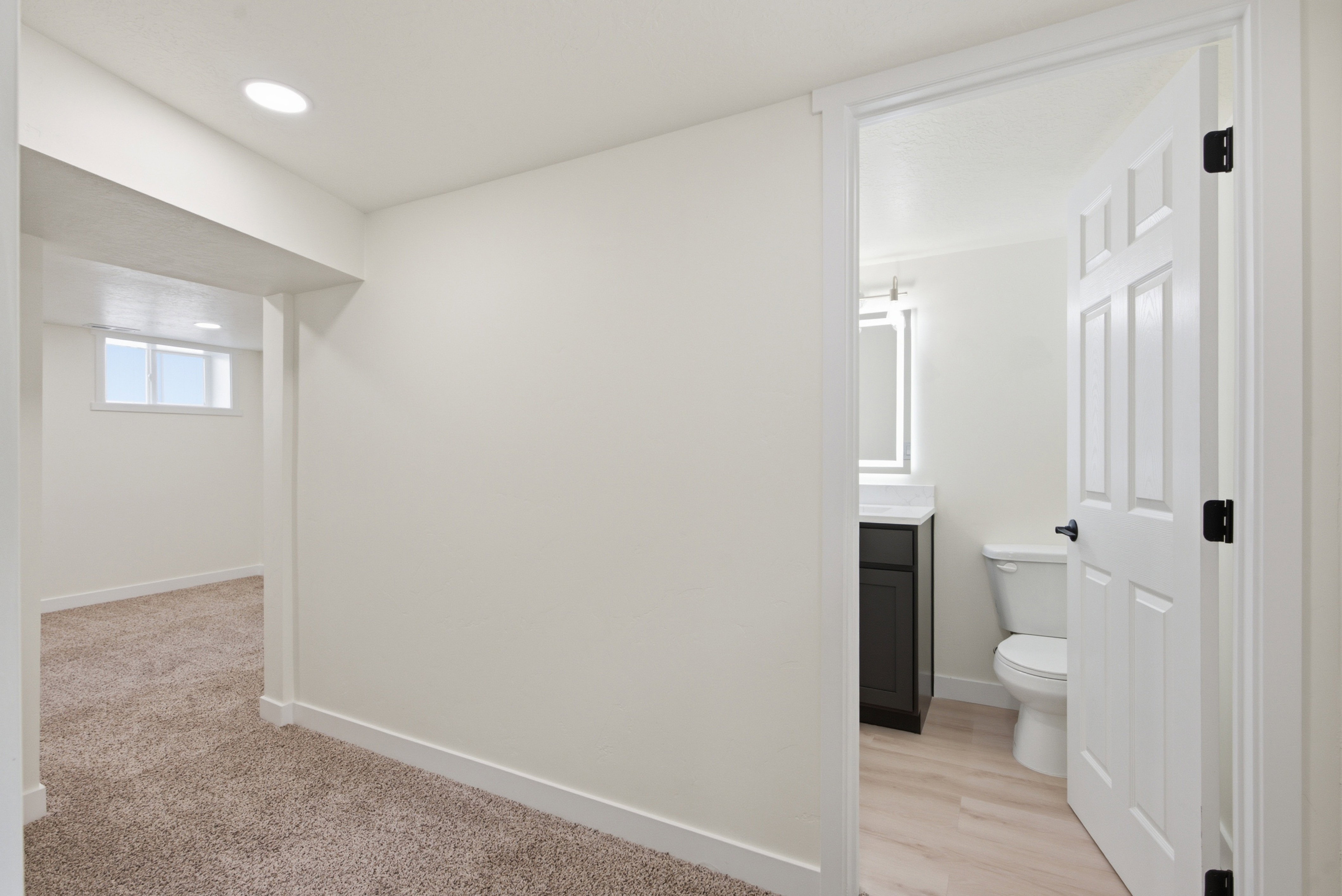 Contemporary bathroom featuring a dark wood-finish vanity with a white countertop, modern illuminated mirror, and light wood-finish flooring