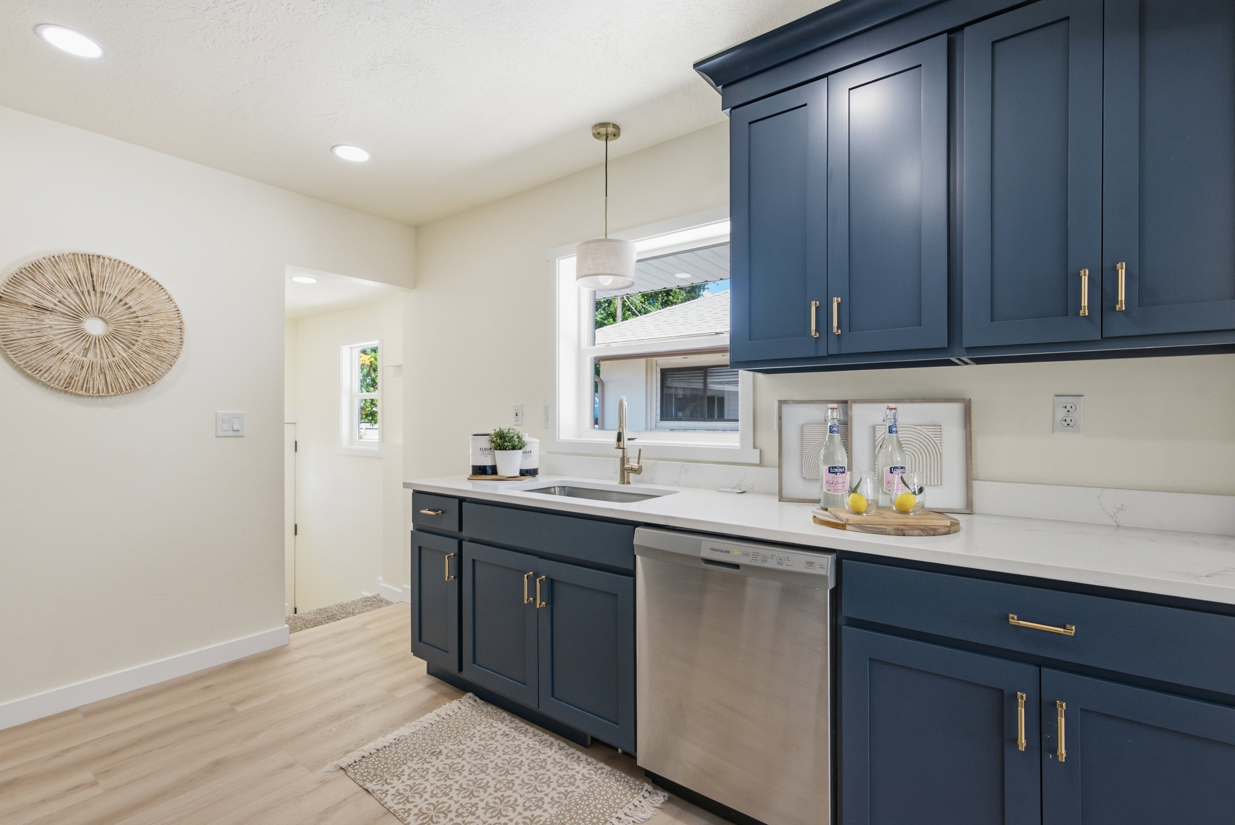 Kitchen featuring blue shaker-style cabinetry with gold-toned hardware, white solid surface countertops, and a stainless steel dishwasher