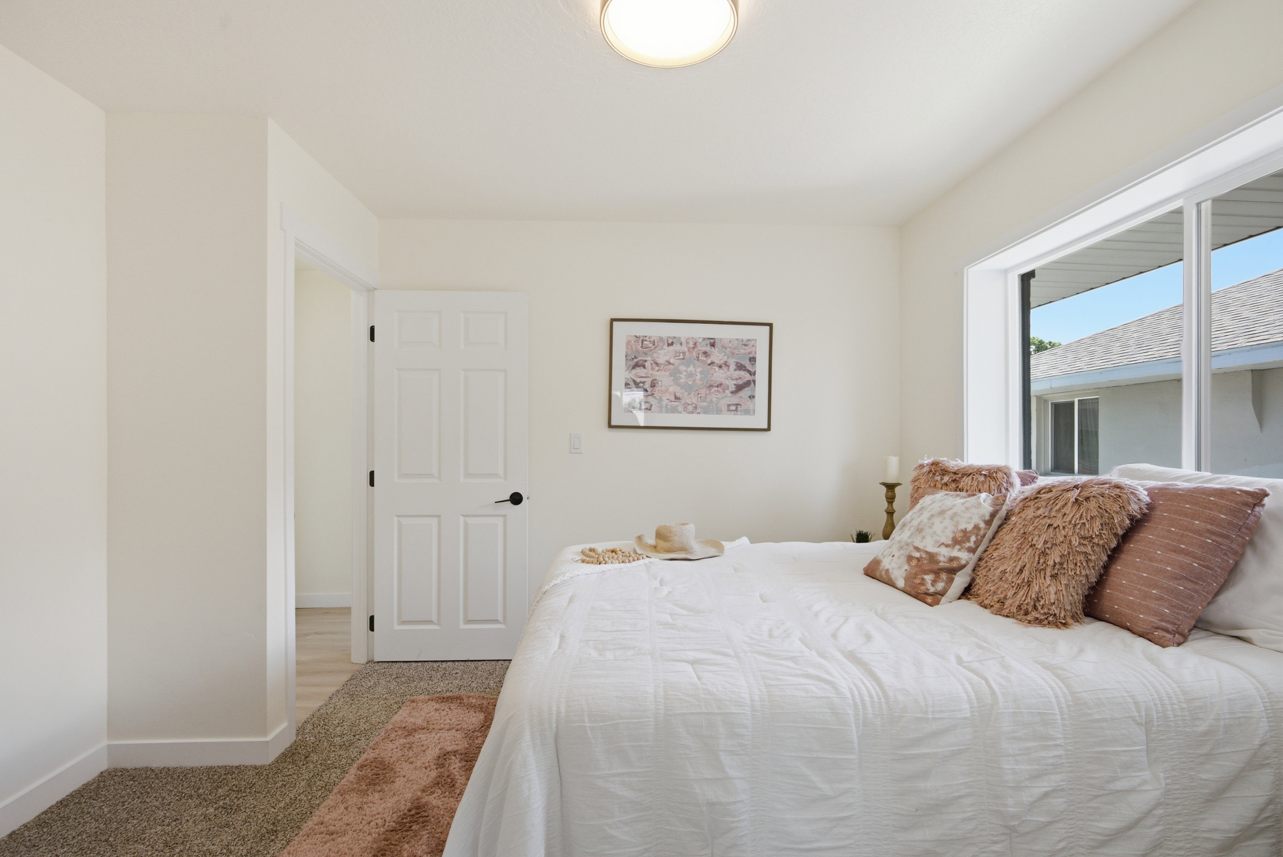 Bright room featuring a large window, textured carpeting, a white paneled door with black hardware, and a semi-flush ceiling light fixture