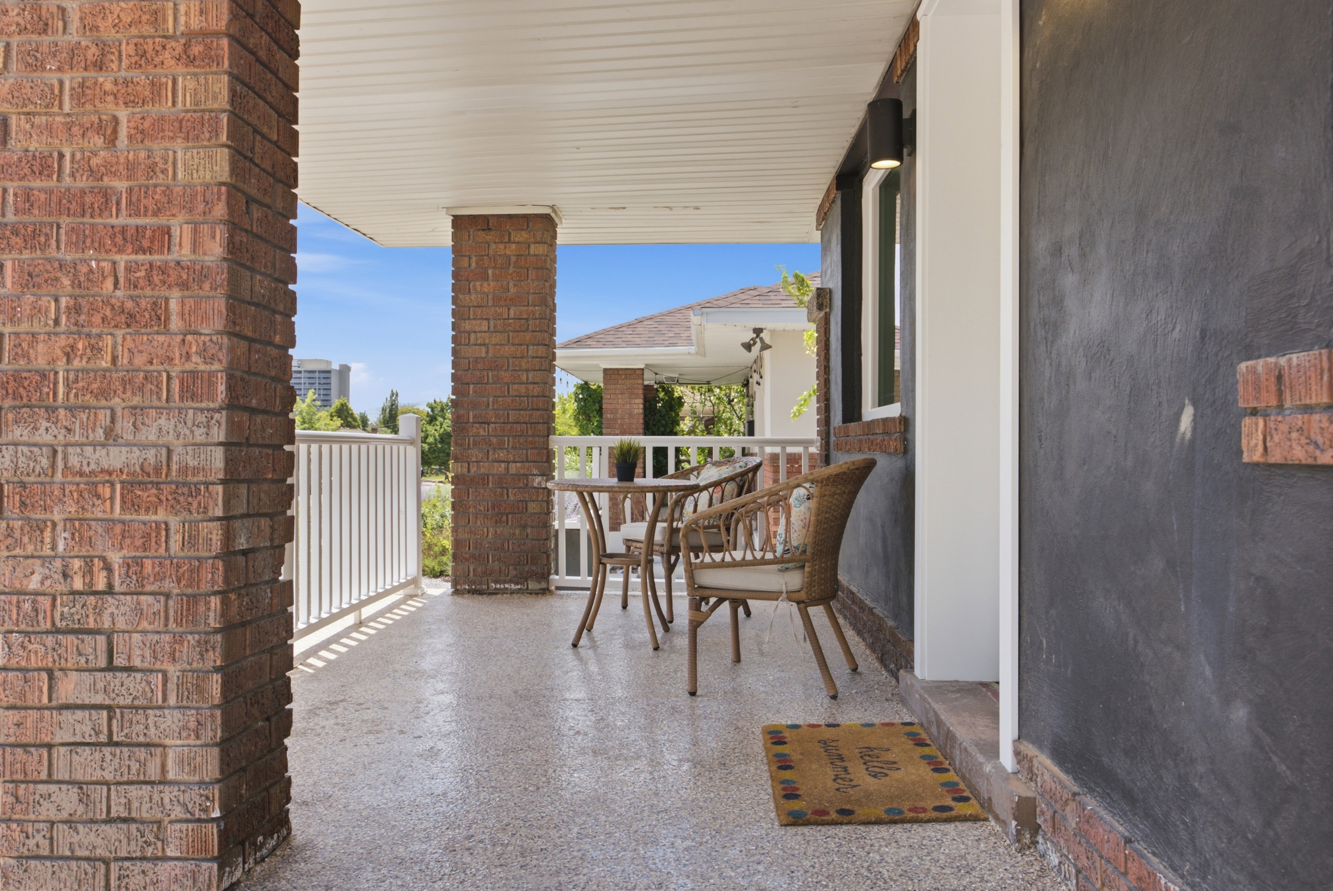 Covered porch featuring brick support columns, white railing, and a textured concrete floor