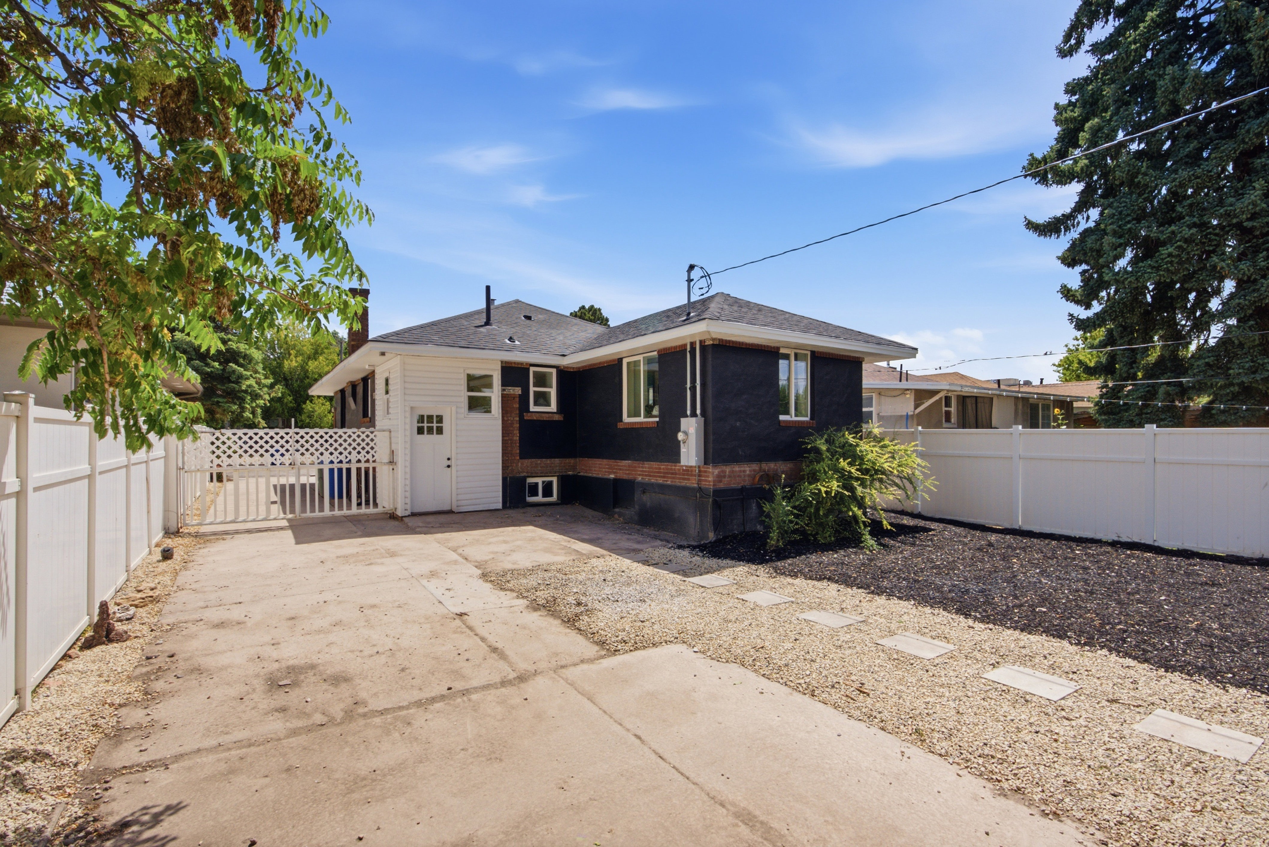 Rear exterior featuring white vinyl fencing, a concrete driveway, and a gravel walkway with stepping stones
