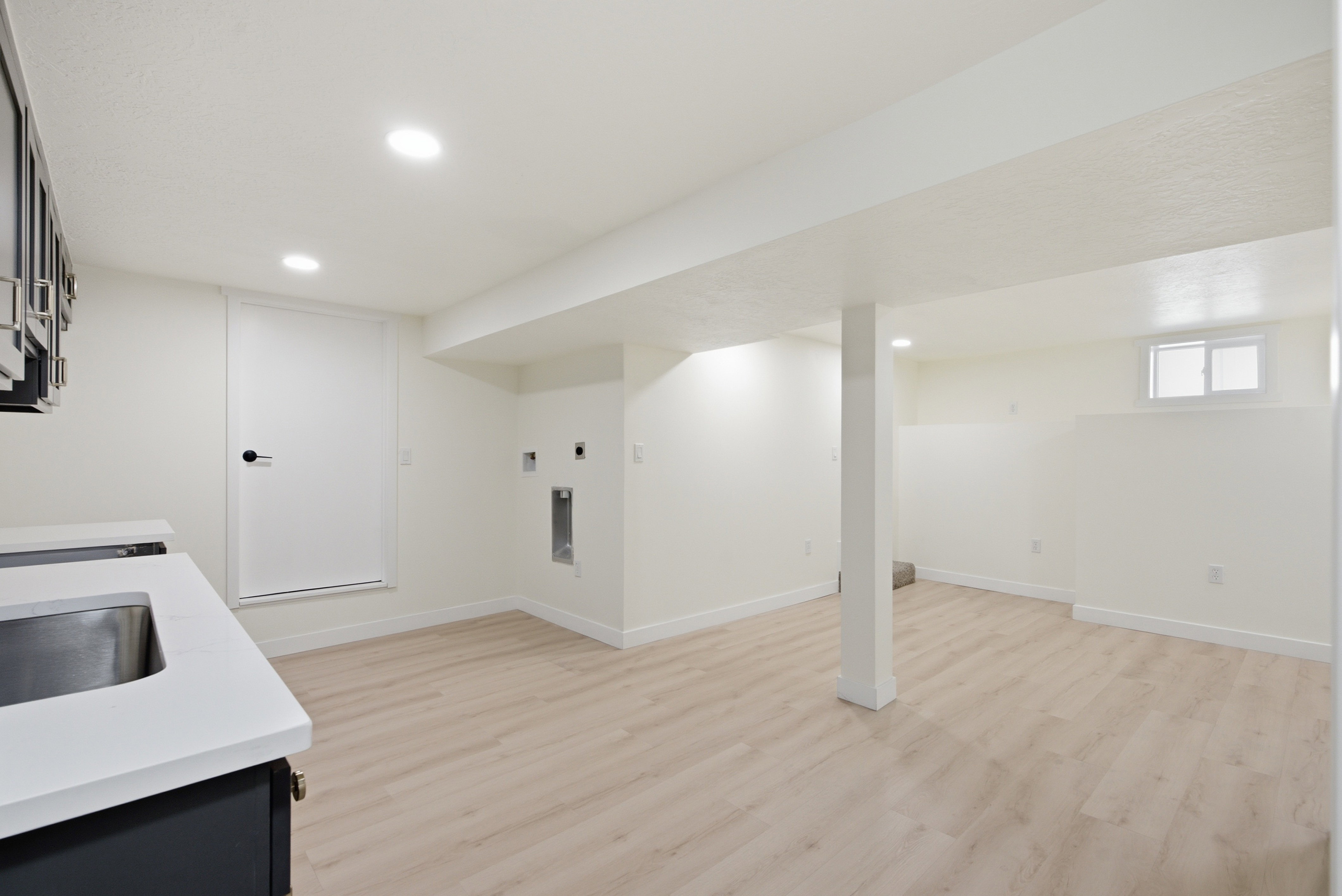 Spacious lower level featuring light wood-finish flooring, recessed lighting, and a utility sink with a solid surface countertop