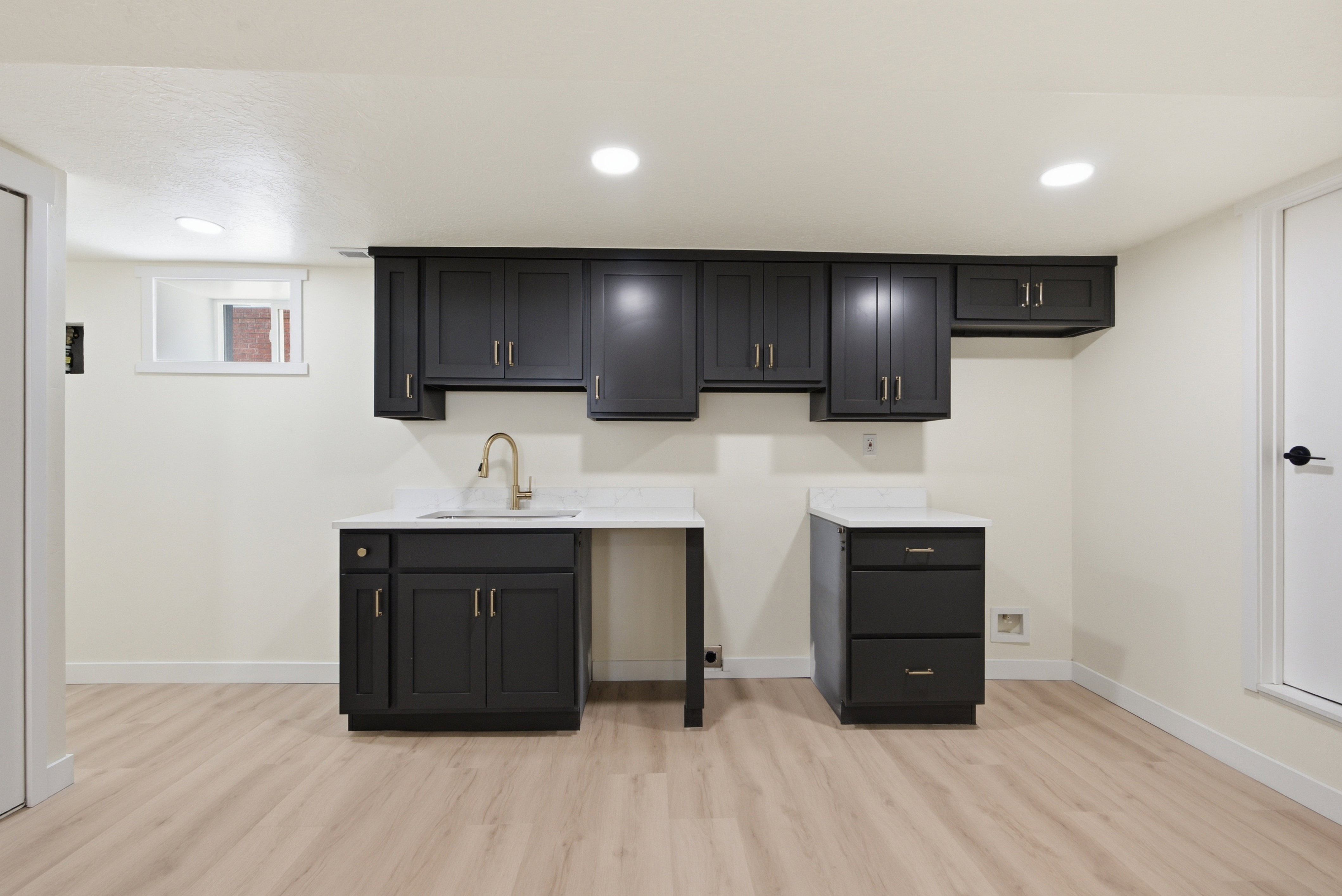 Lower-level space featuring wood-finish flooring, recessed lighting, and a built-in wet bar with dark cabinetry, a white countertop, and a gold-tone faucet