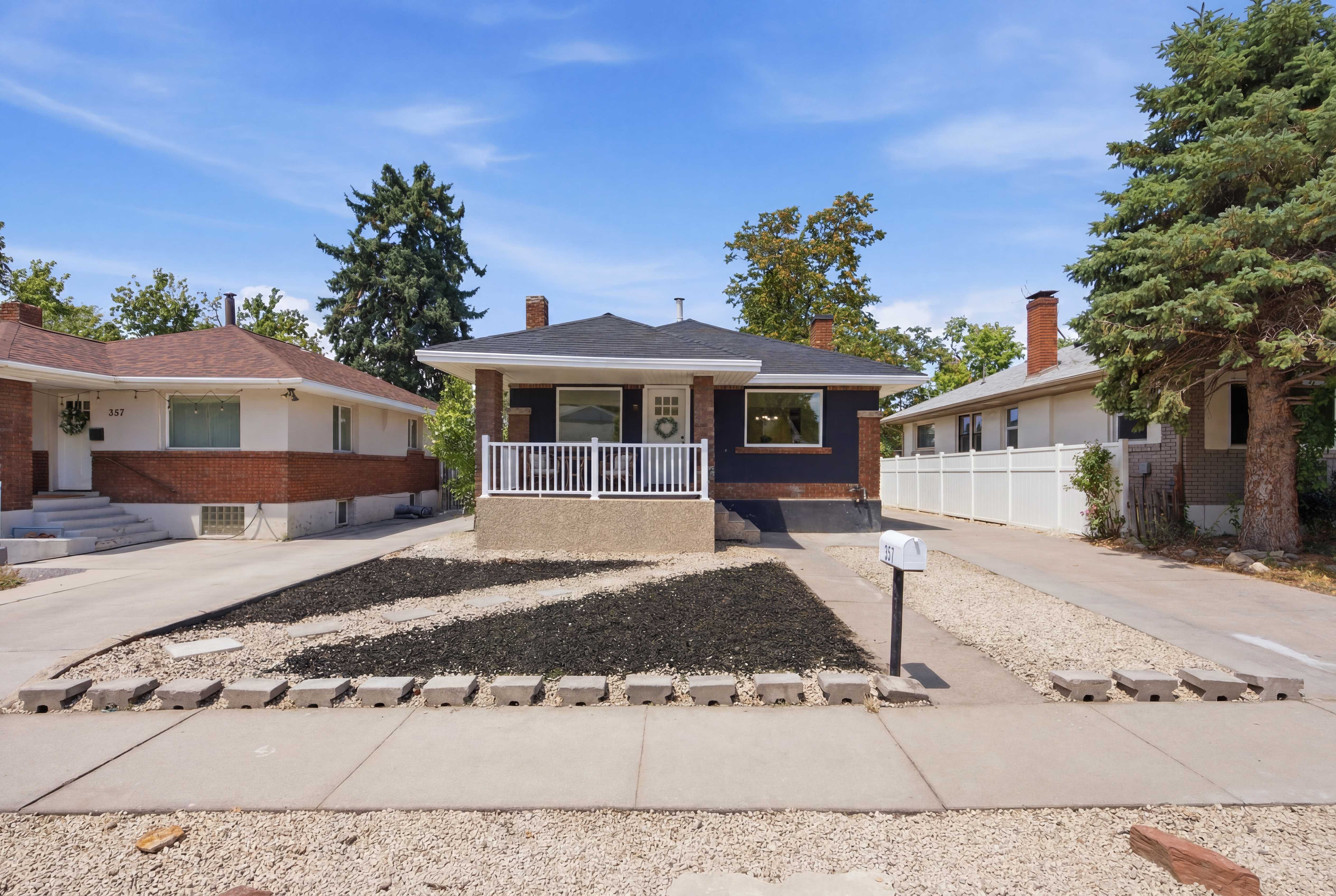 Ranch-style residence featuring a dark facade with contrasting white trim, a covered front porch with white railing, and a dark shingle roof