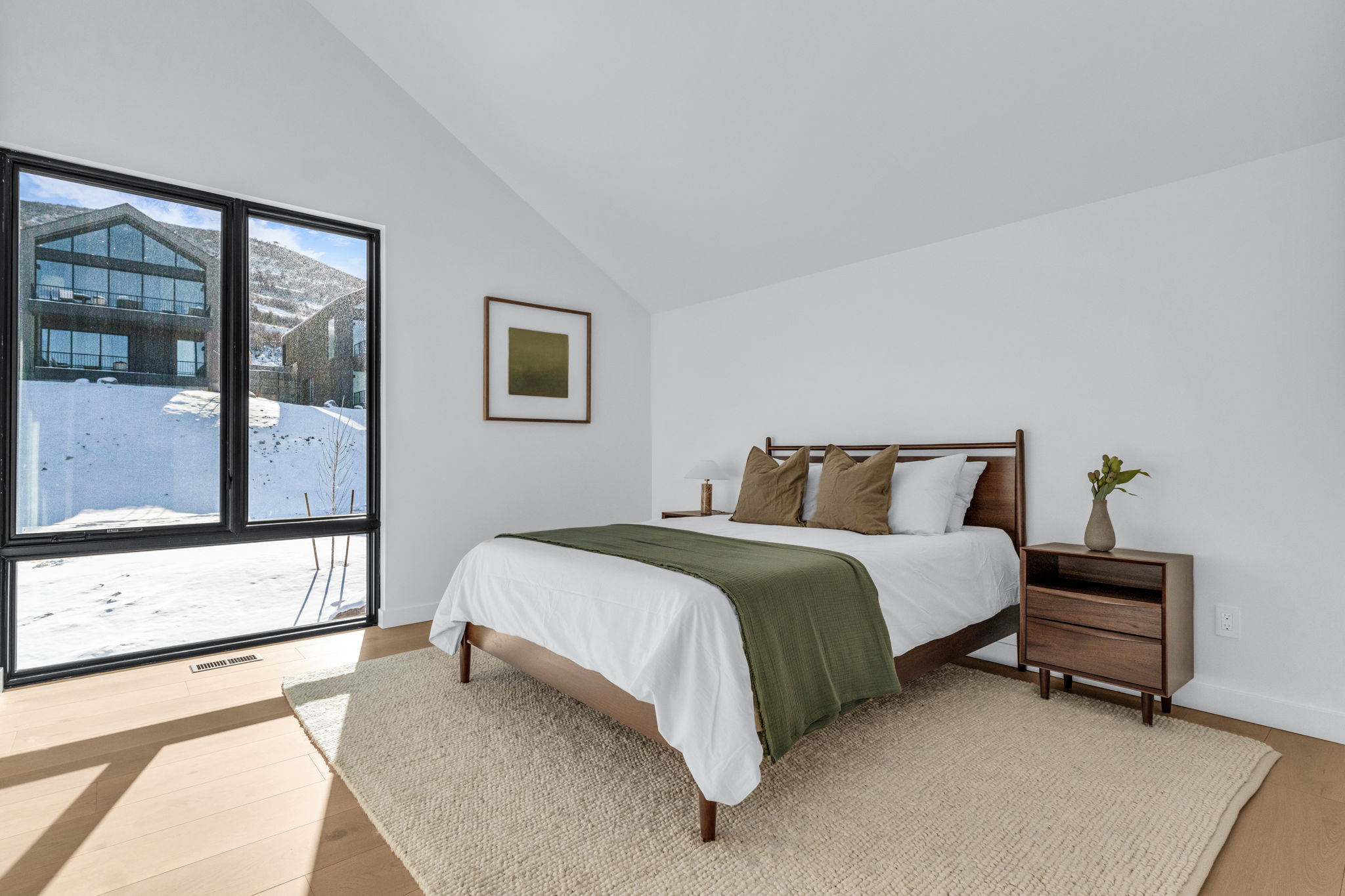 Expansive window feature with black framing, wood-finish flooring, vaulted ceiling, and white wall finishes