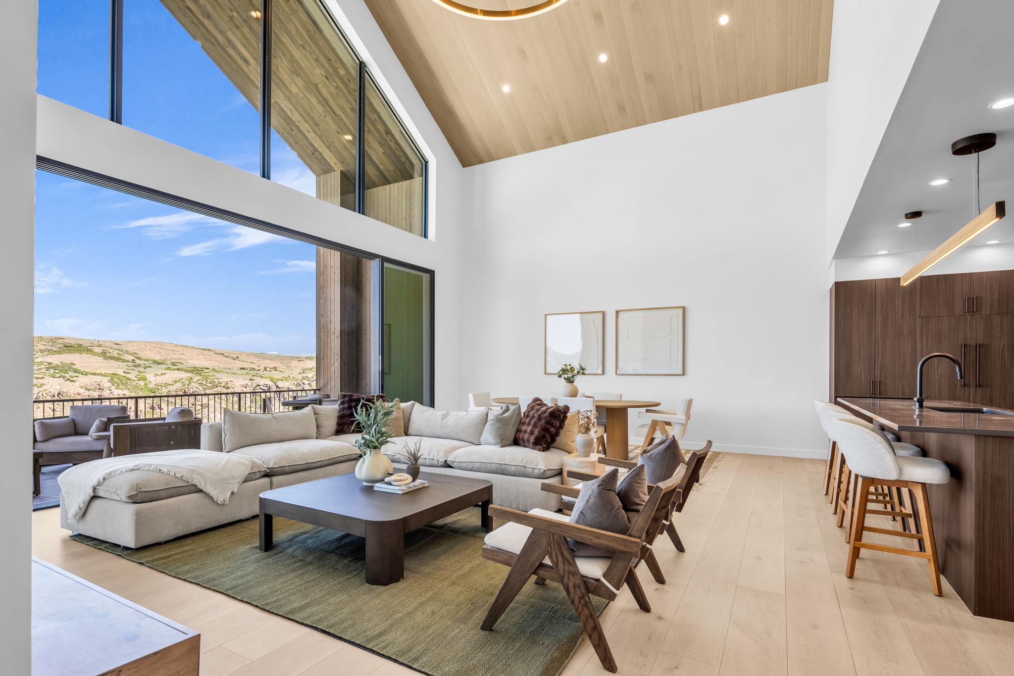 Open-concept living space with vaulted wood-paneled ceilings, light wood-finish flooring, and expansive floor-to-ceiling windows