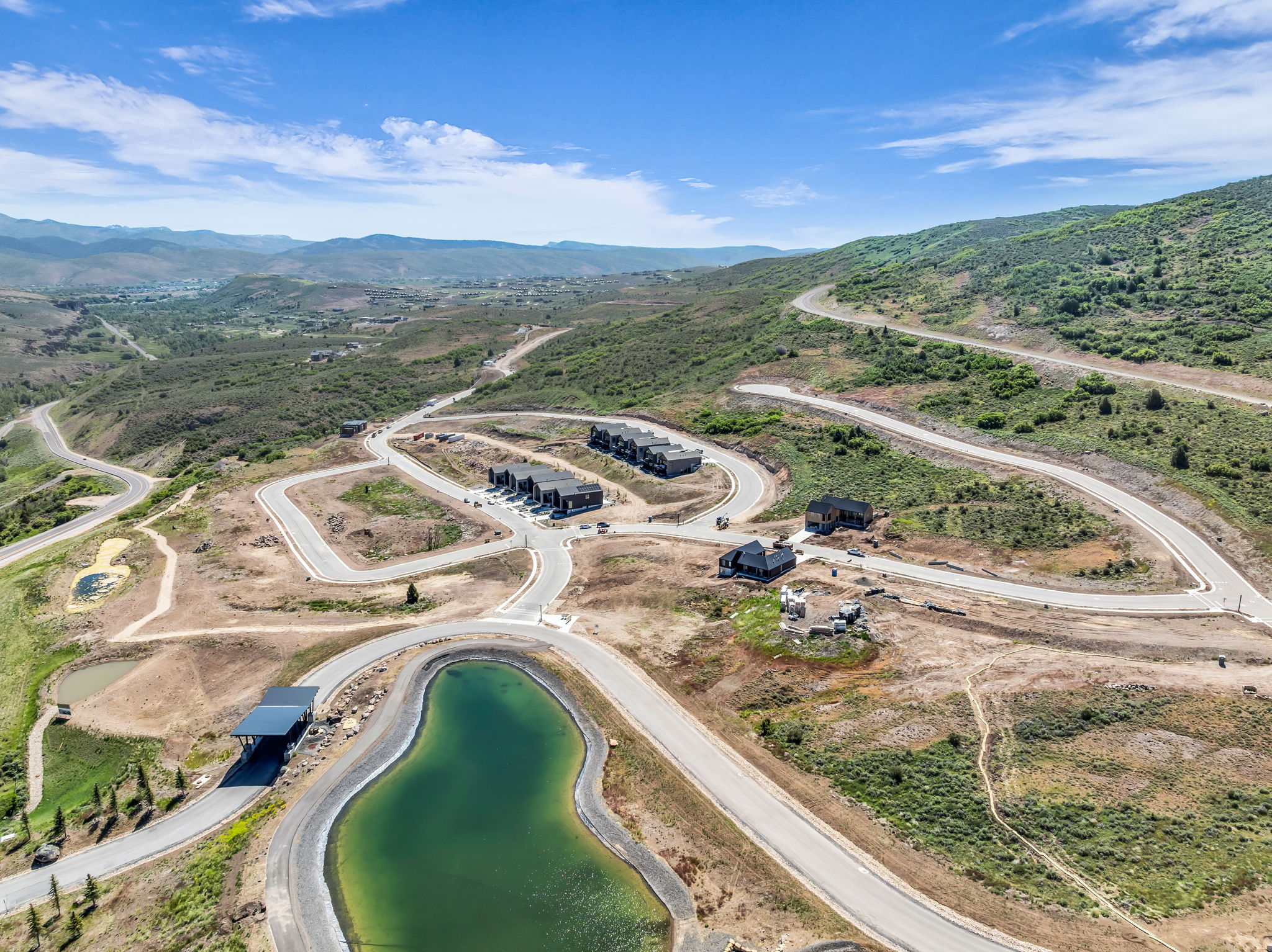 Hillside development featuring a water feature, paved roads, and multiple structures under construction