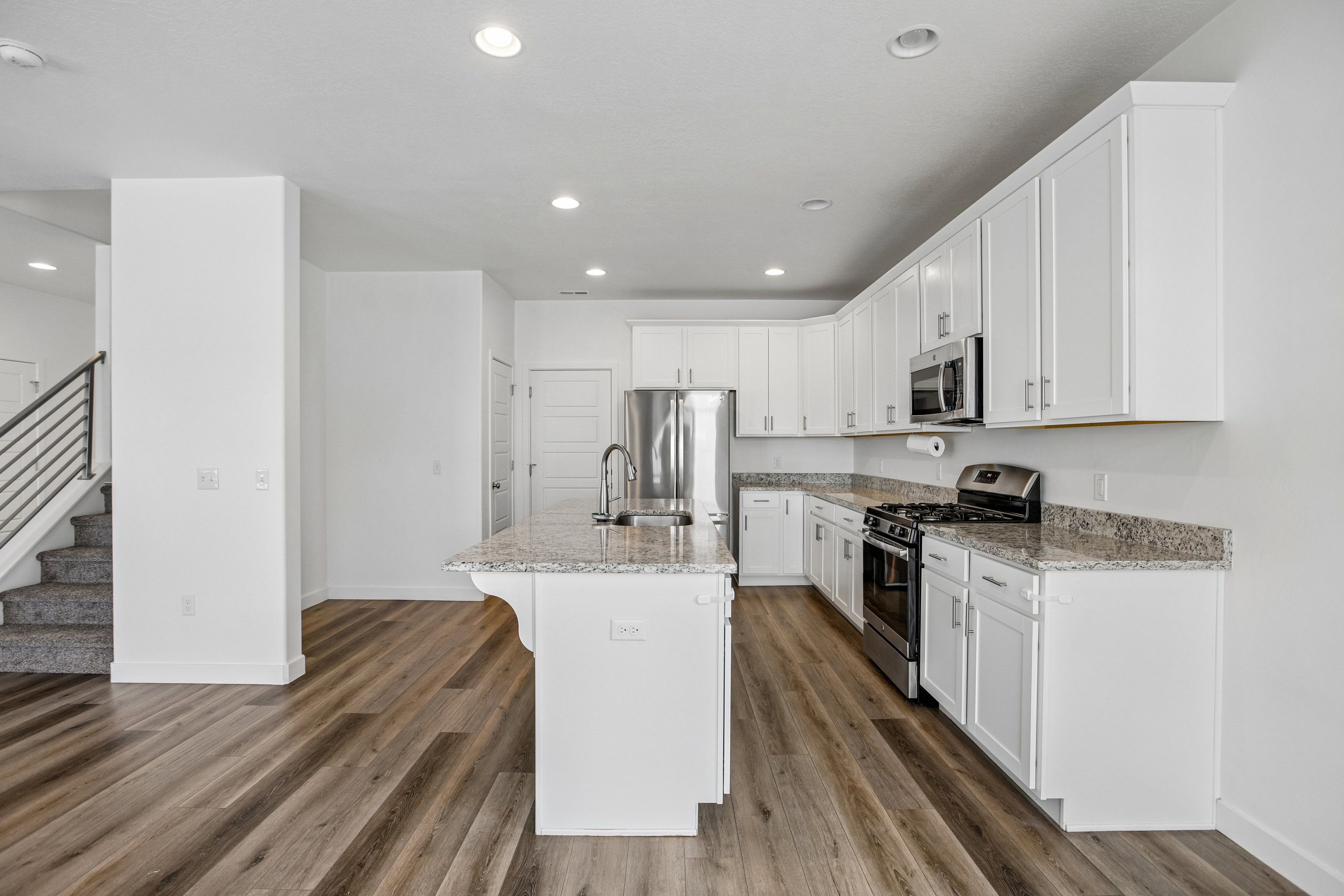 Open-concept kitchen featuring an island with a sink, white cabinetry, stainless steel appliances, and granite countertops