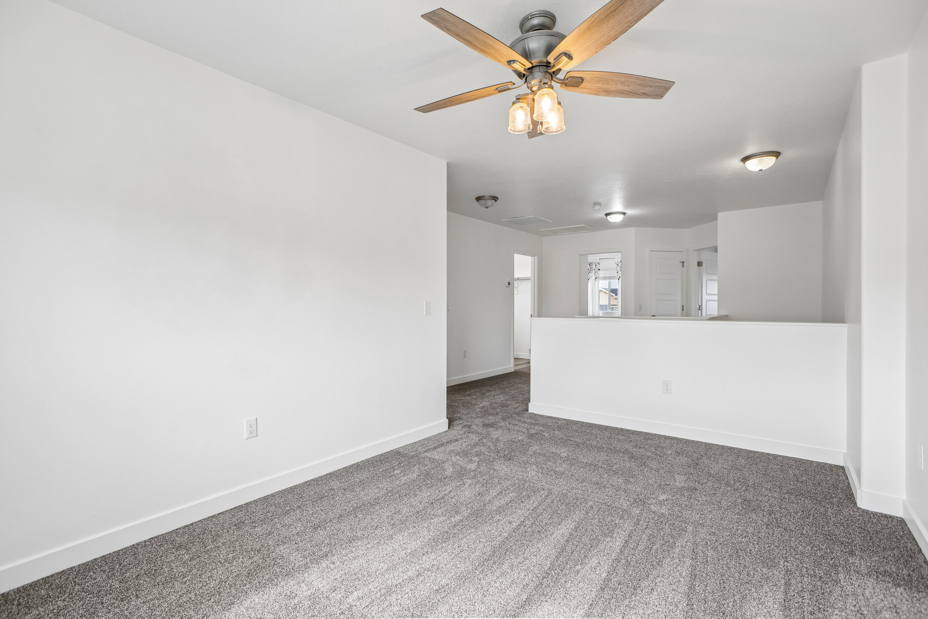Spacious room featuring gray textured carpeting, white walls, a multi-speed ceiling fan with integrated lighting, and multiple recessed light fixtures