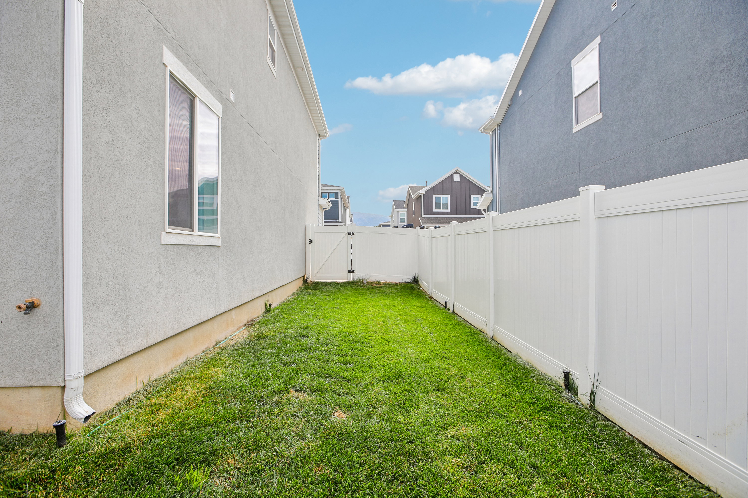 Side yard with a grass lawn, white vinyl fencing, and a white vinyl gate