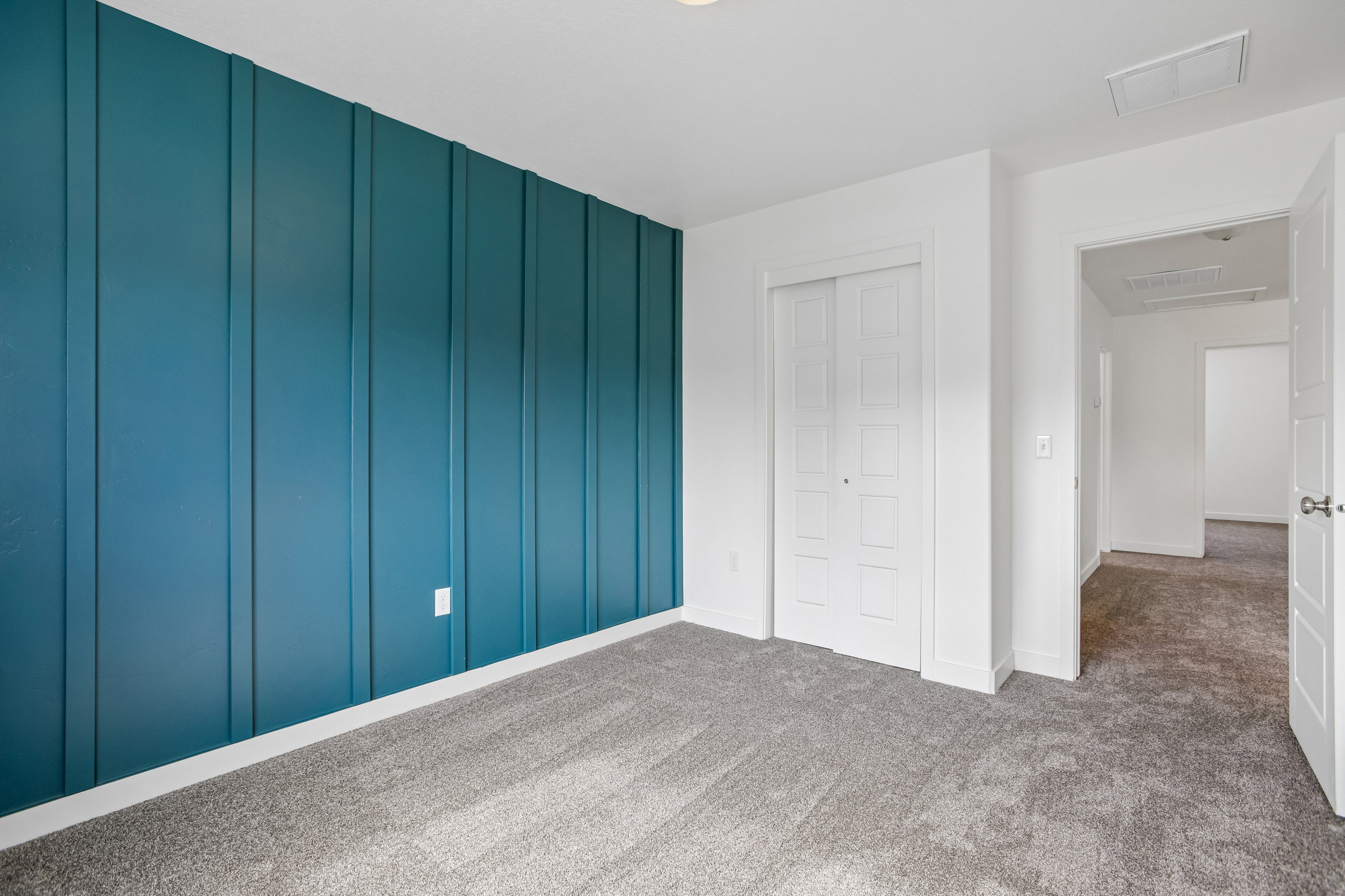 Bedroom featuring a decorative teal accent wall with vertical paneling, plush gray carpeting, and white baseboards