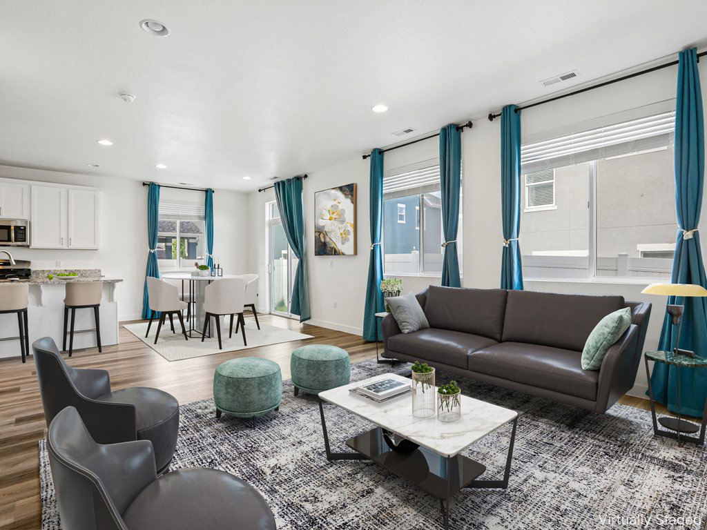 Open-concept living space featuring wood-finish flooring, recessed lighting, and large windows with blinds