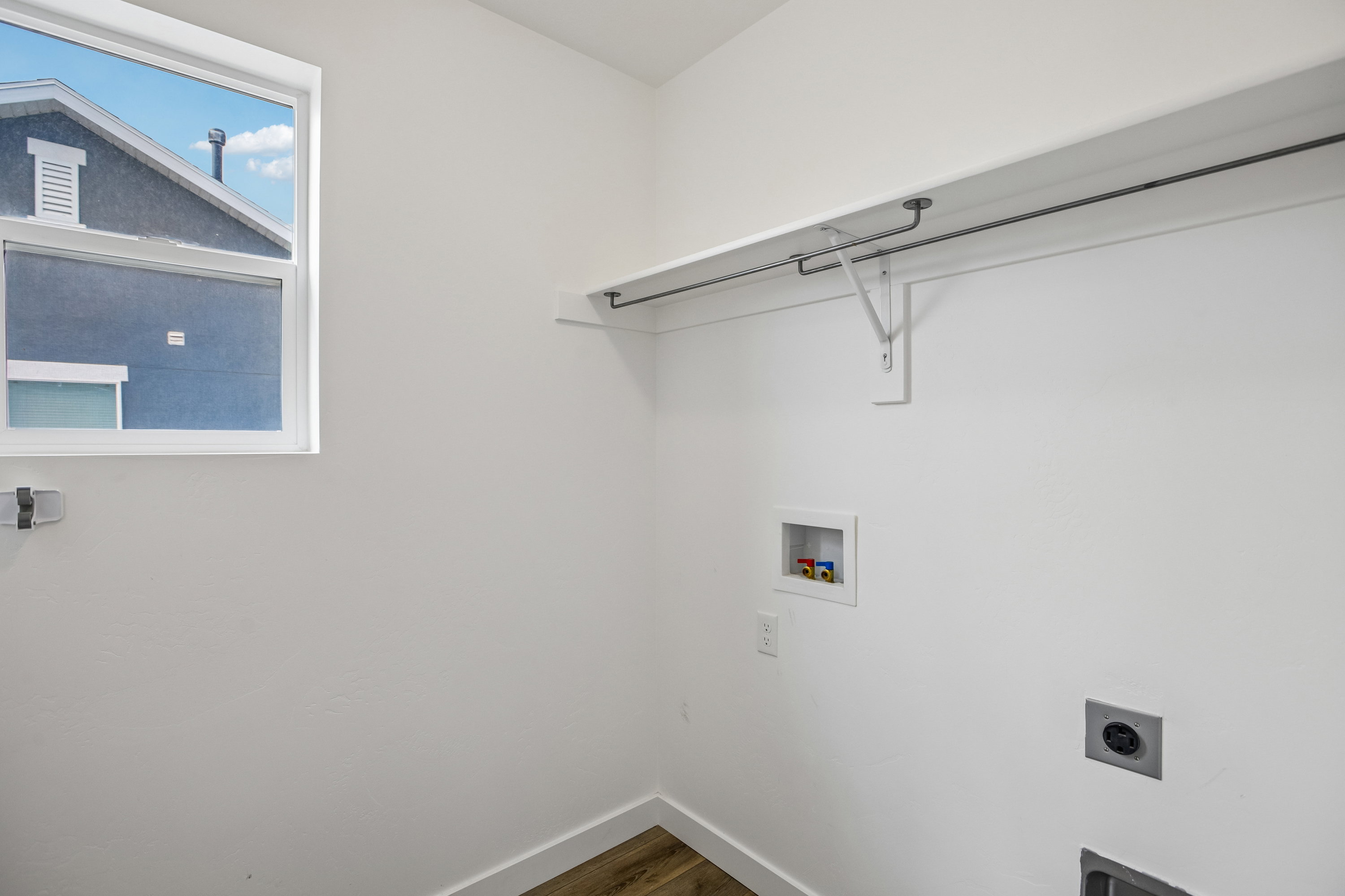 Utility room with a window, white walls, wood-finish flooring, and a built-in shelving unit with a hanging rod