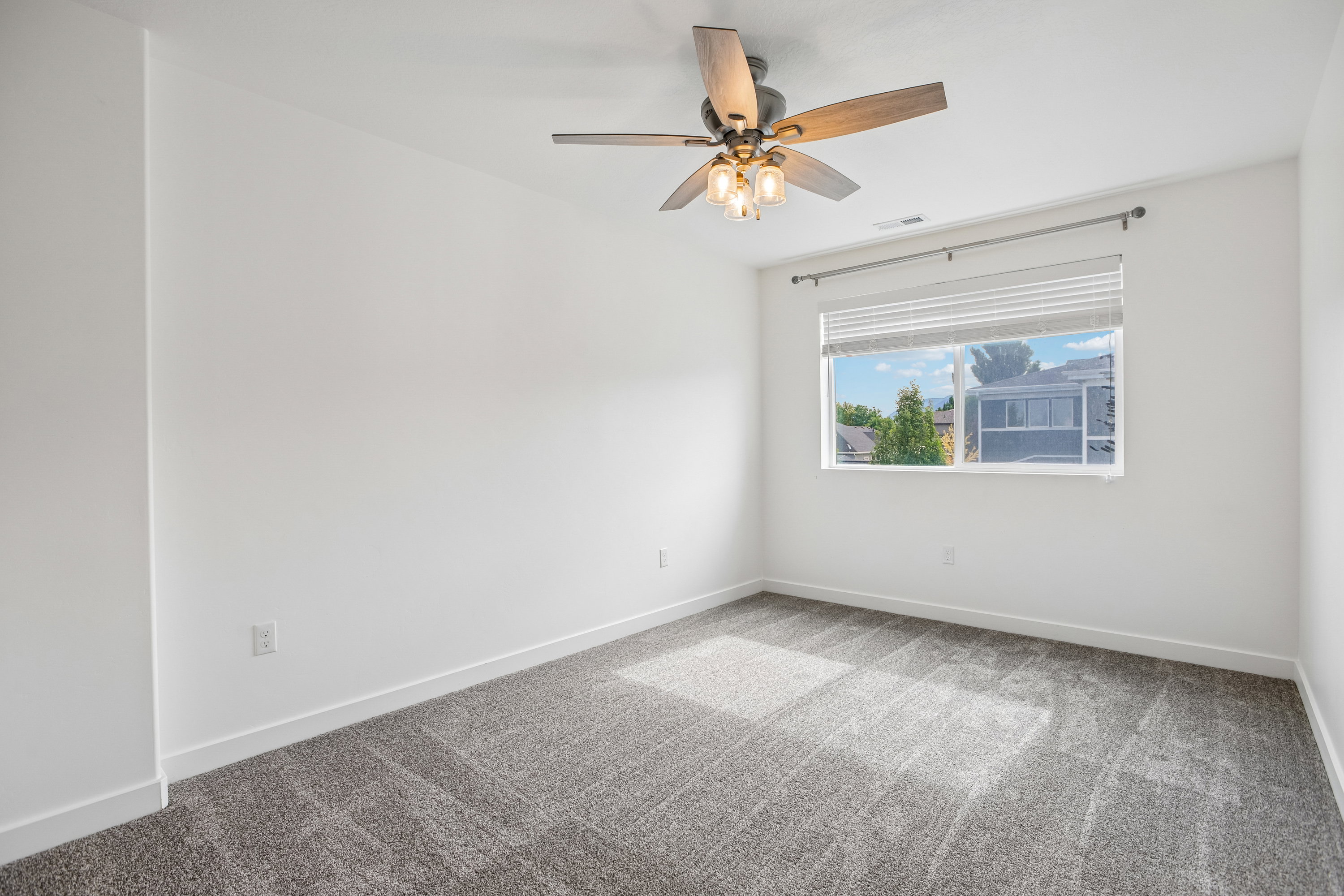 Room featuring white walls, gray carpet, a window with blinds, and a ceiling fan with integrated lighting