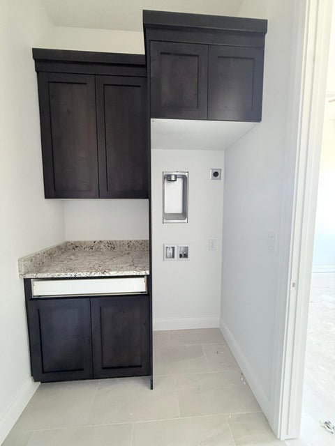 Laundry area featuring dark wood-finish cabinetry, a stone countertop, and light-toned tile flooring