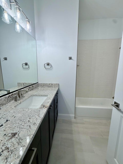 Bathroom featuring a vanity with a white granite countertop, undermount sink, dark wood-finish cabinetry, and a full-width mirror