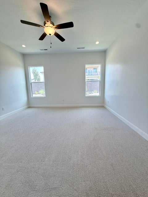 Spacious room featuring neutral carpeting, white walls, two windows, recessed lighting, and a ceiling fan with integrated light