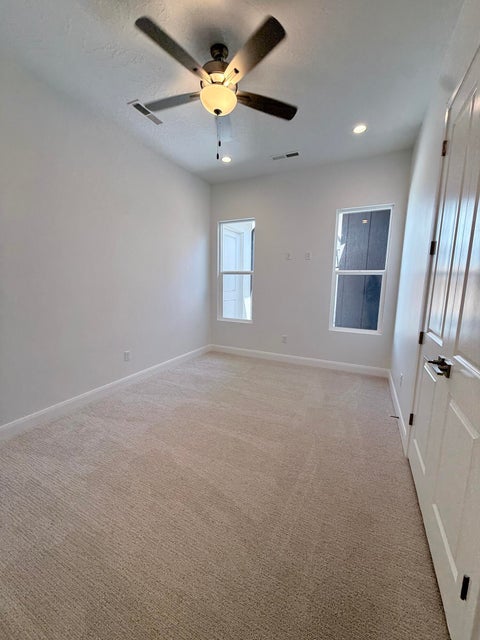Neutral tone carpeted room featuring a ceiling fan with integrated lighting, two recessed ceiling lights, and two windows