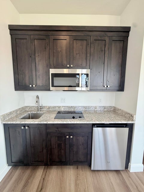 Compact kitchen area featuring dark wood-finish cabinetry, granite-style countertops, an undermount stainless steel sink, a stainless steel microwave, and an integrated two-burner cooktop