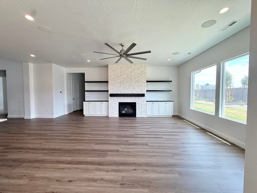 Spacious living area featuring wood-finish flooring, a stone-clad fireplace with a dark wood mantel, built-in shelving, white cabinetry, and large windows