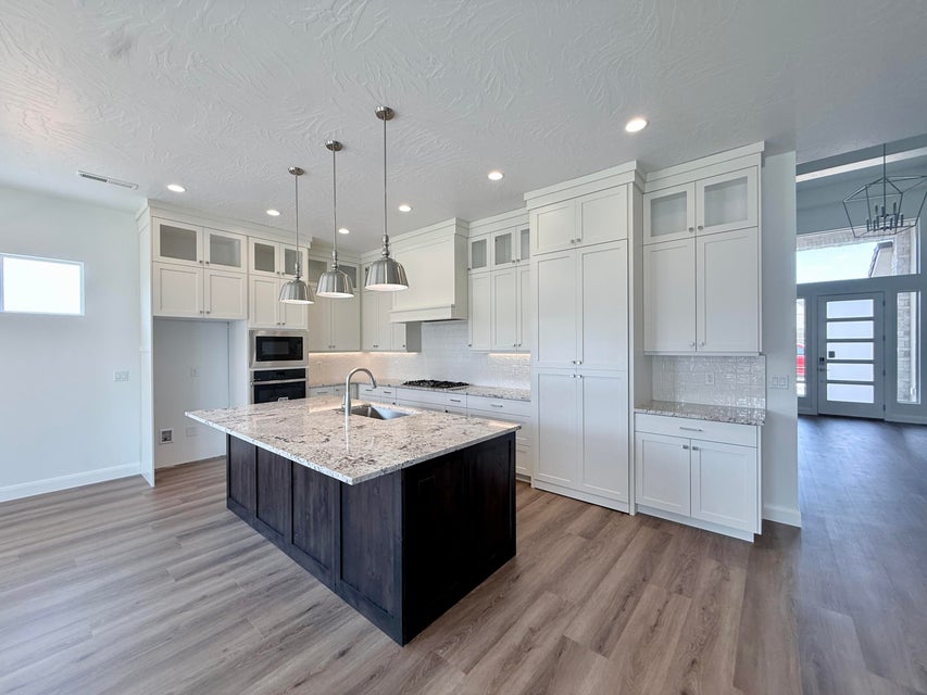 Gourmet kitchen featuring a dark wood-finish island with a light-toned countertop, white cabinetry with upper glass-front accents, stainless steel appliances, and wood-finish flooring