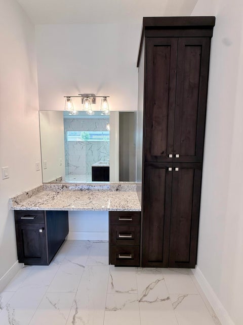 Vanity area featuring a spacious countertop, dark wood-finish cabinetry, a built-in storage tower, and white tile flooring