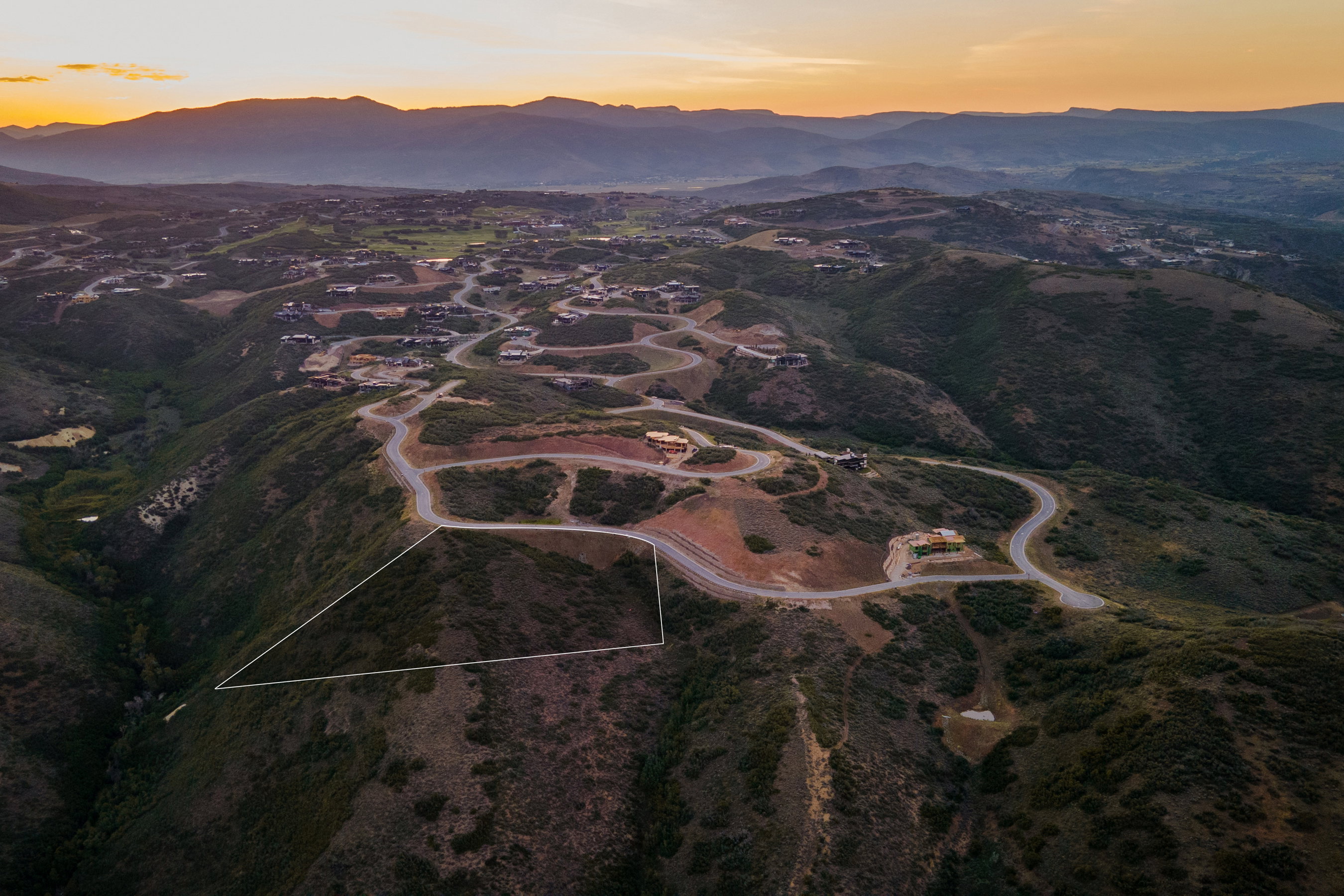 Expansive mountain terrain with a defined property outline, featuring winding paved roads and distant residential structures