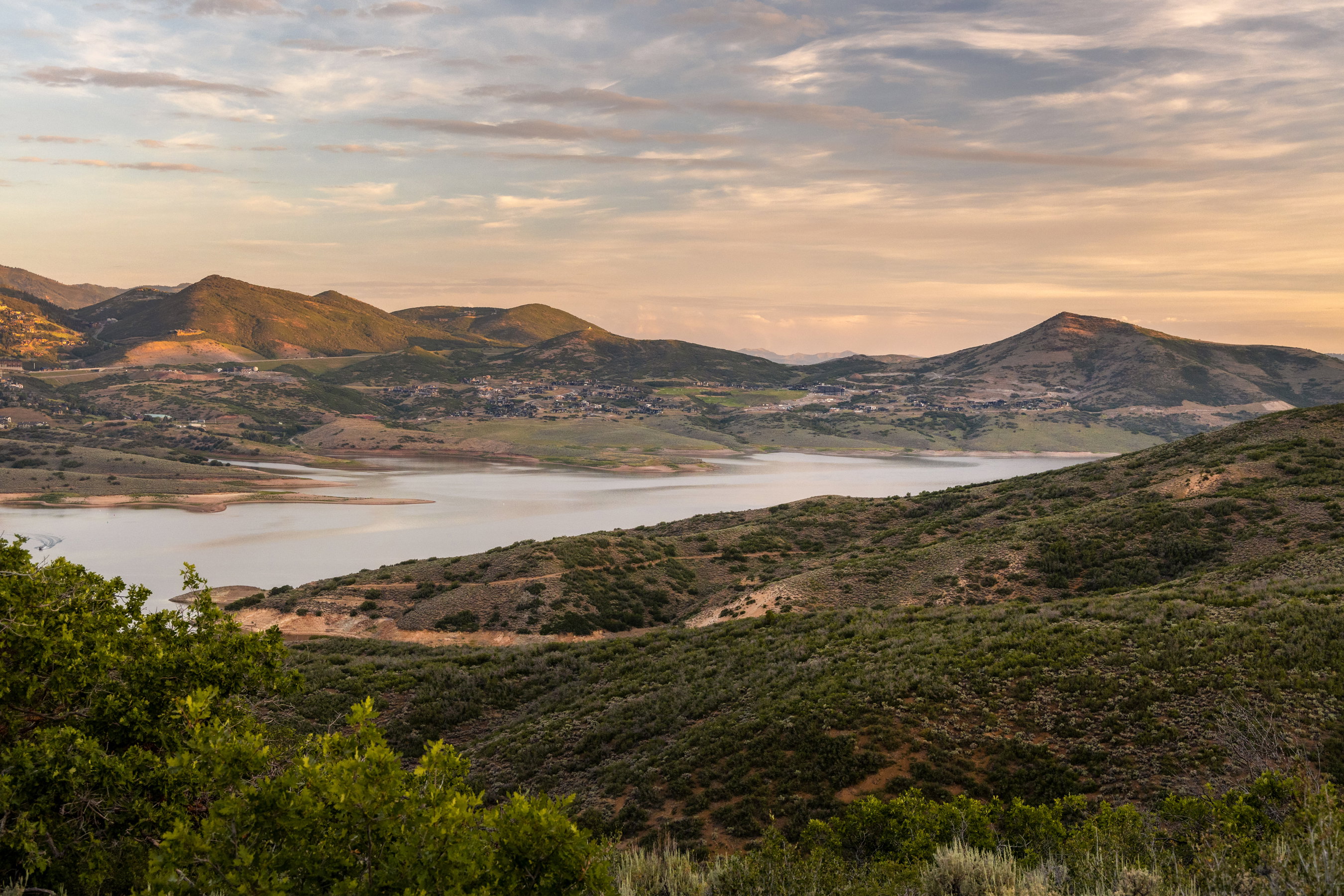 Expansive mountainous landscape featuring a large body of water, rolling hillsides, and distant settlements