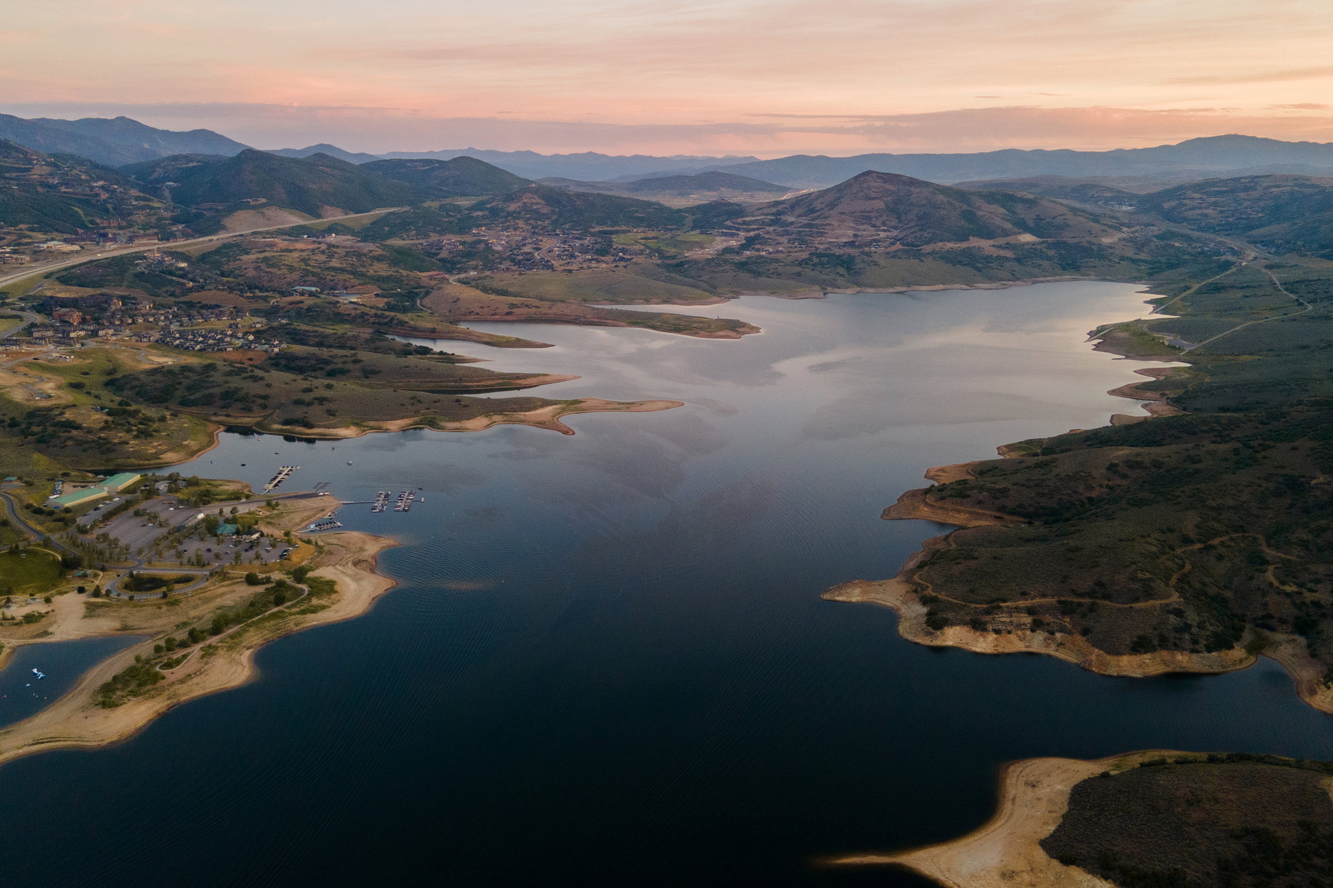 Expansive lake with surrounding land featuring a marina, docks, and nearby mountainous terrain