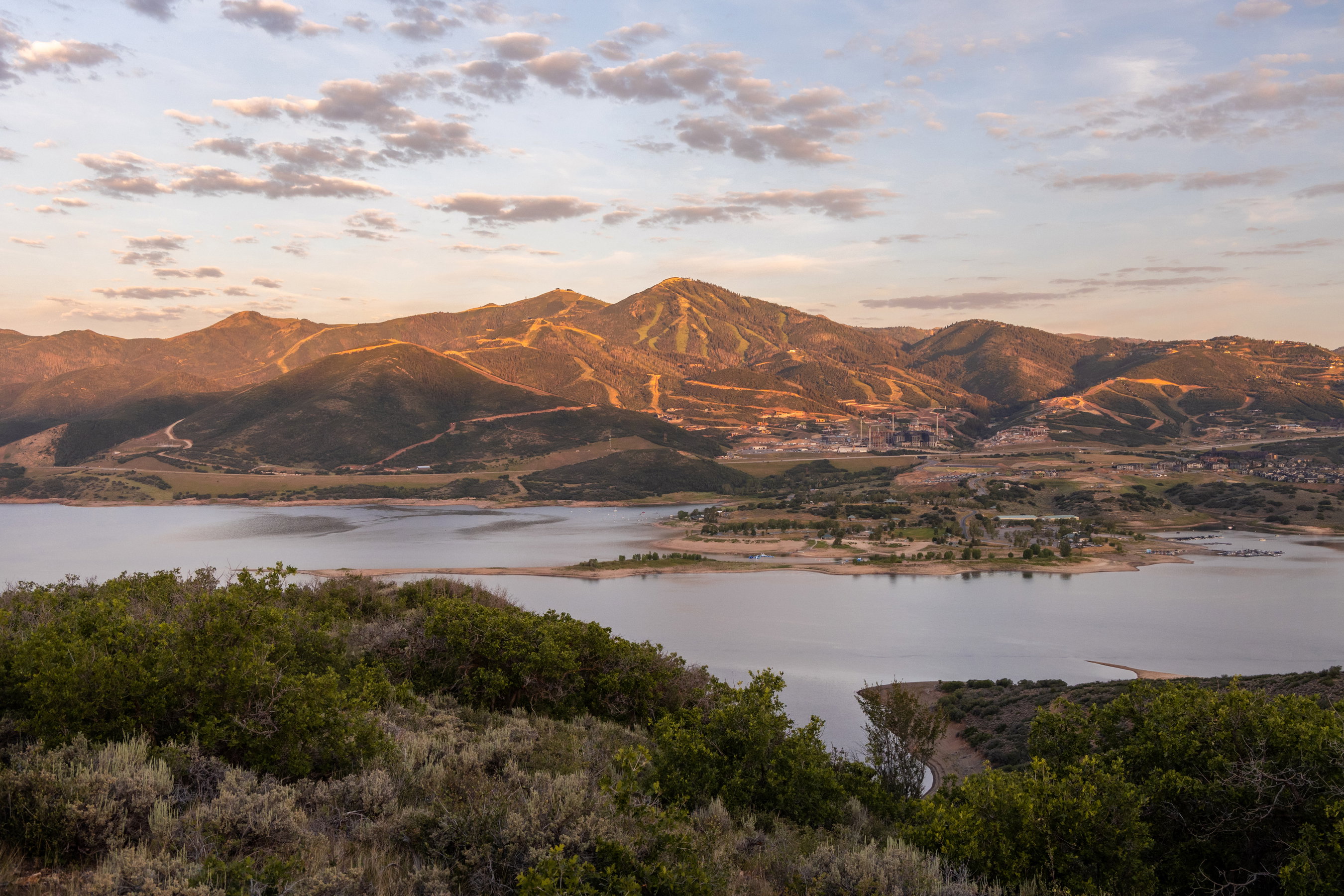 Expansive mountain landscape featuring a large body of water, distant structures, and natural foliage