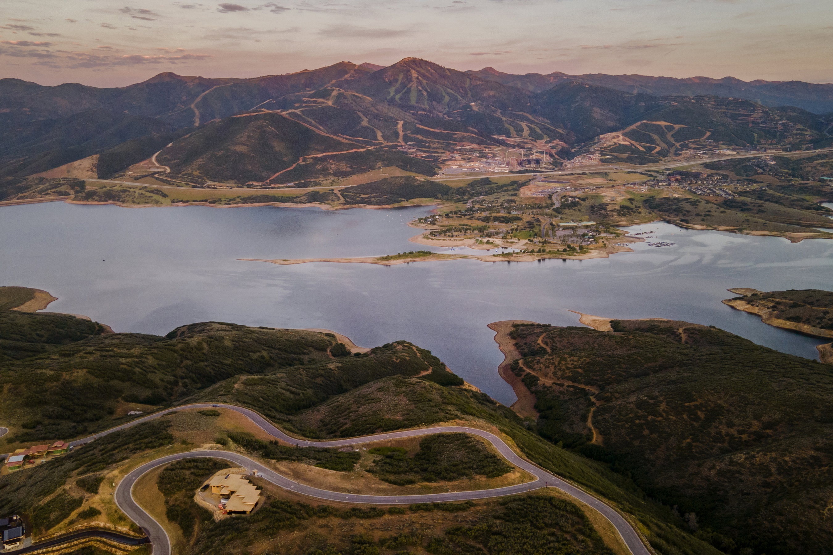 Sweeping aerial perspective encompassing a large body of water, distant mountains, and a winding road