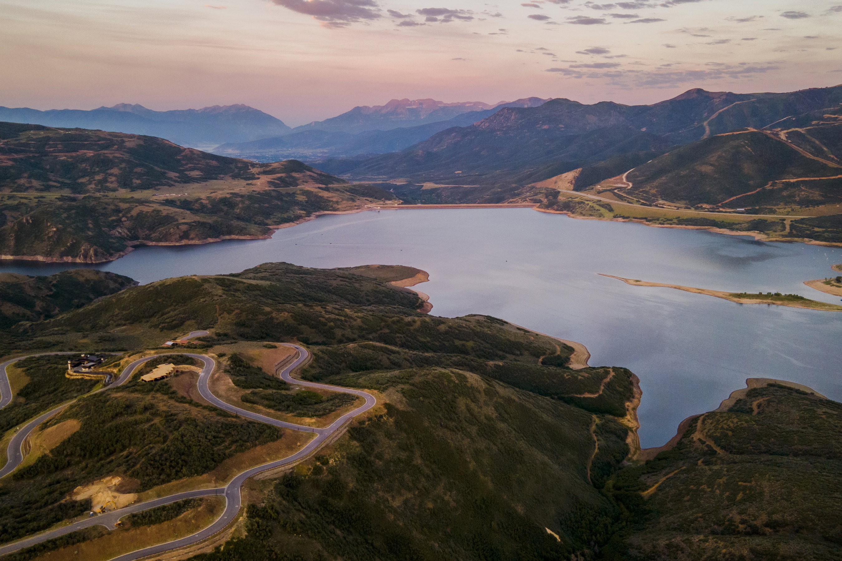 Expansive mountain landscape featuring a large lake, winding roads, and distant peaks