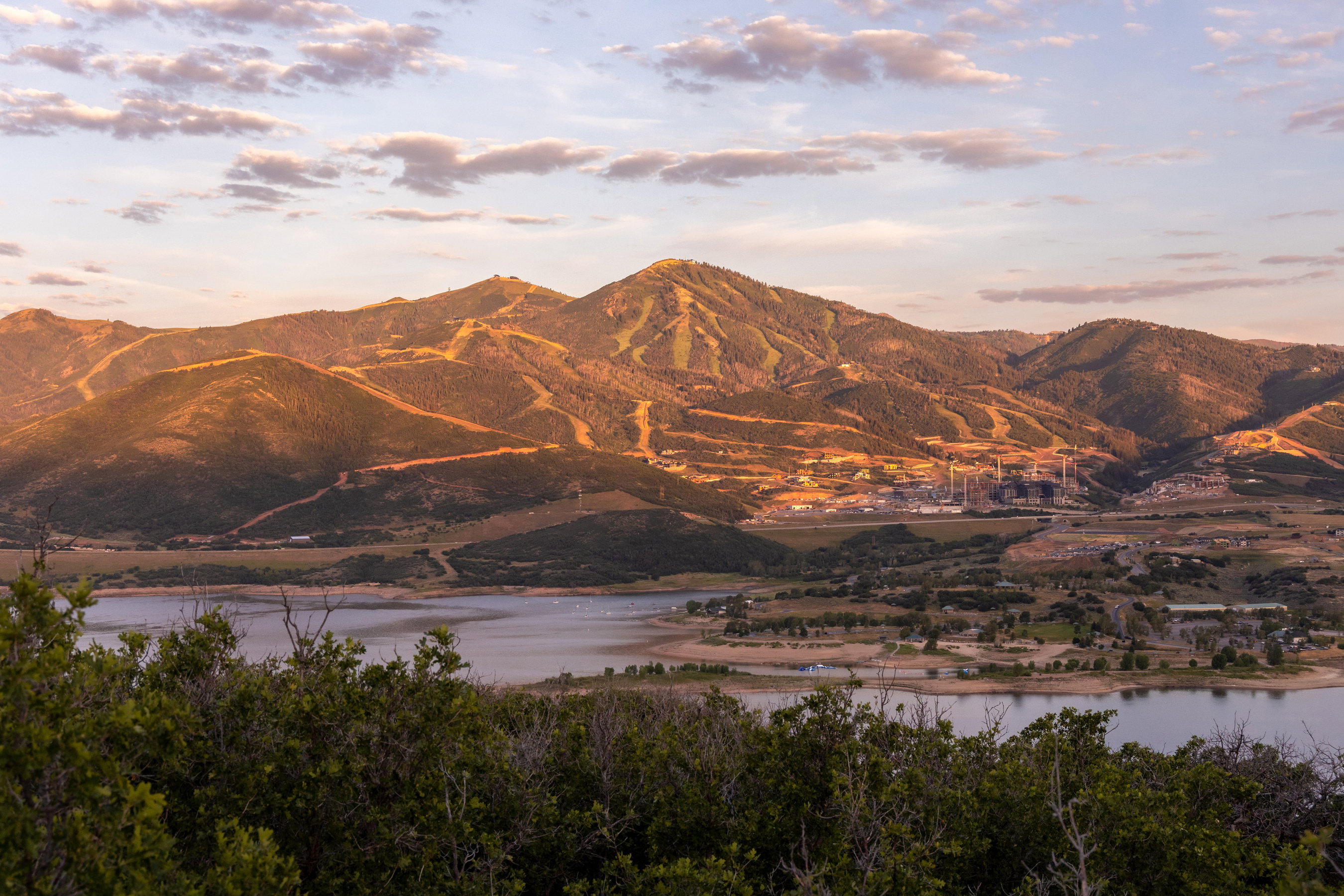 Expansive mountain and lake scenery featuring ski runs, distant structures, and natural foliage