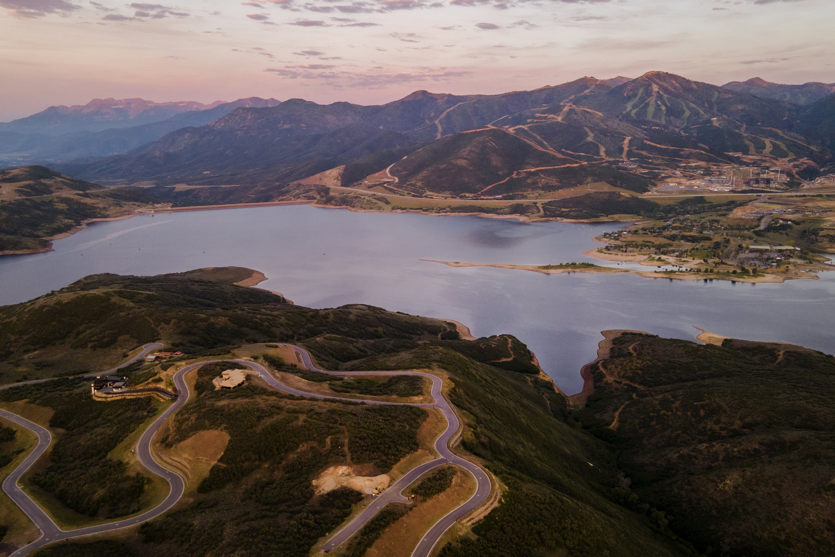 Expansive mountain landscape featuring a large body of water, meandering roads, and distant ski slopes
