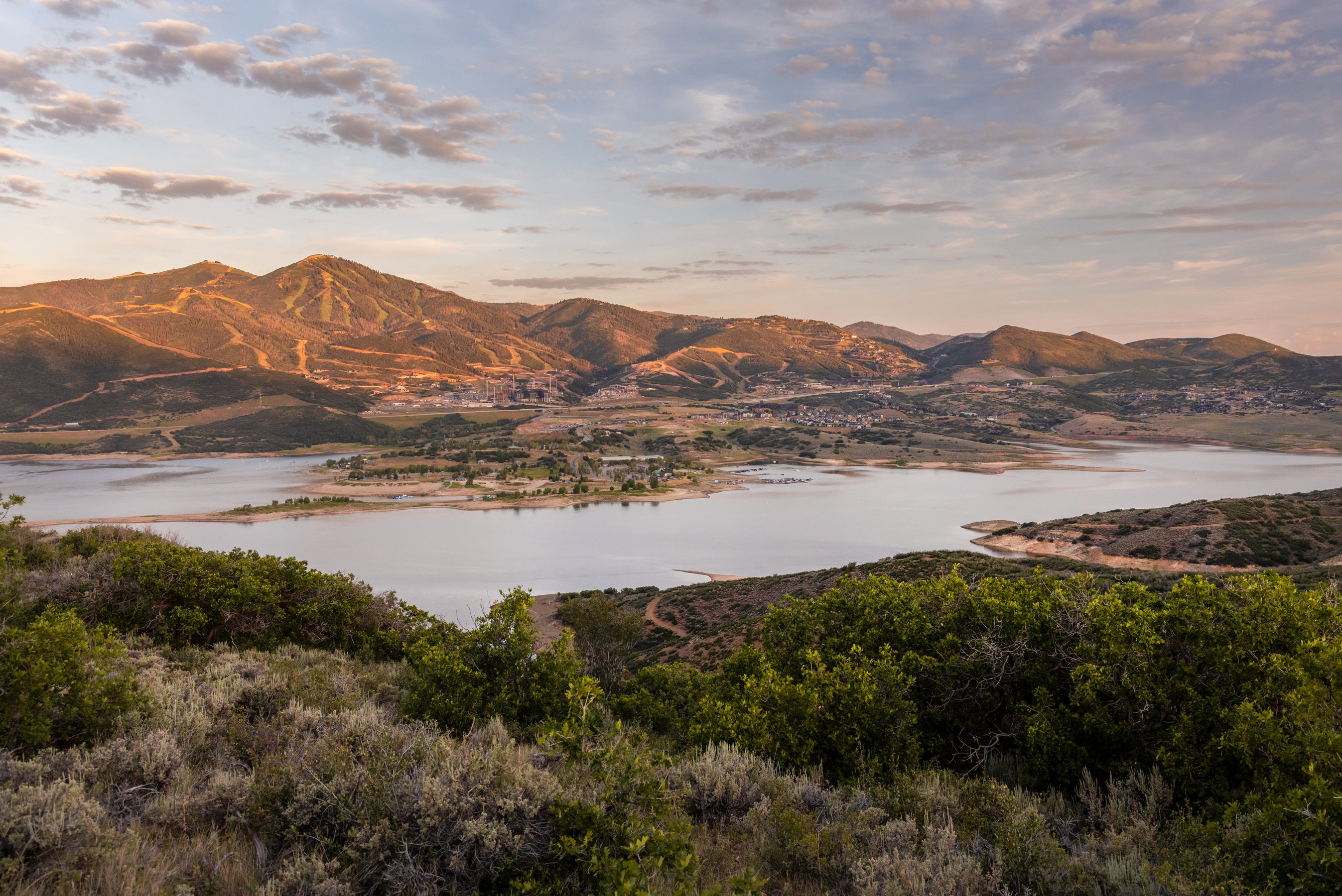 Expansive mountain landscape featuring a large body of water, distant hills, and varied natural vegetation