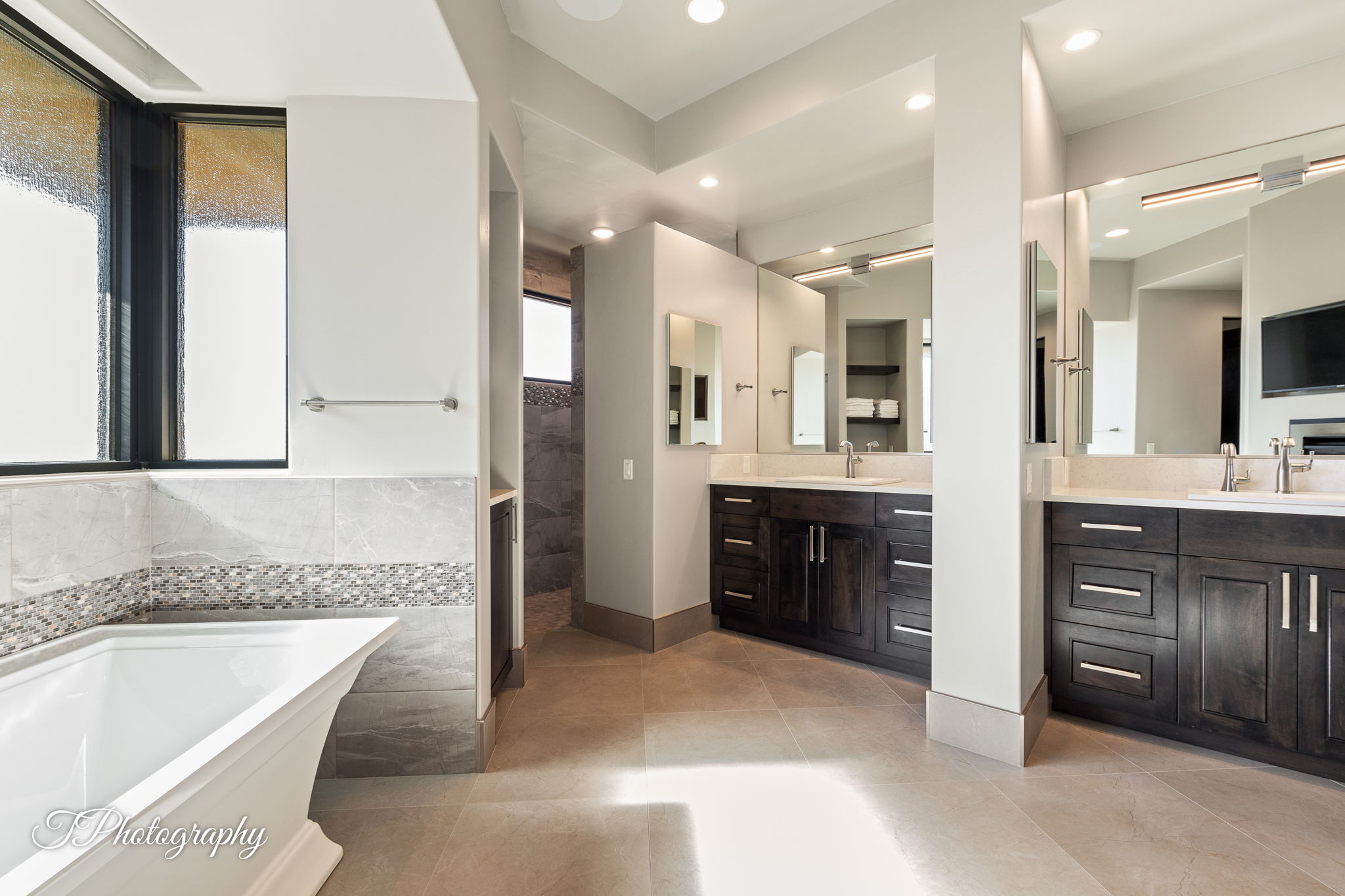 Contemporary bathroom featuring a freestanding soaking tub, twin vanity stations with dark wood cabinetry, light-toned countertops, and integrated lighting