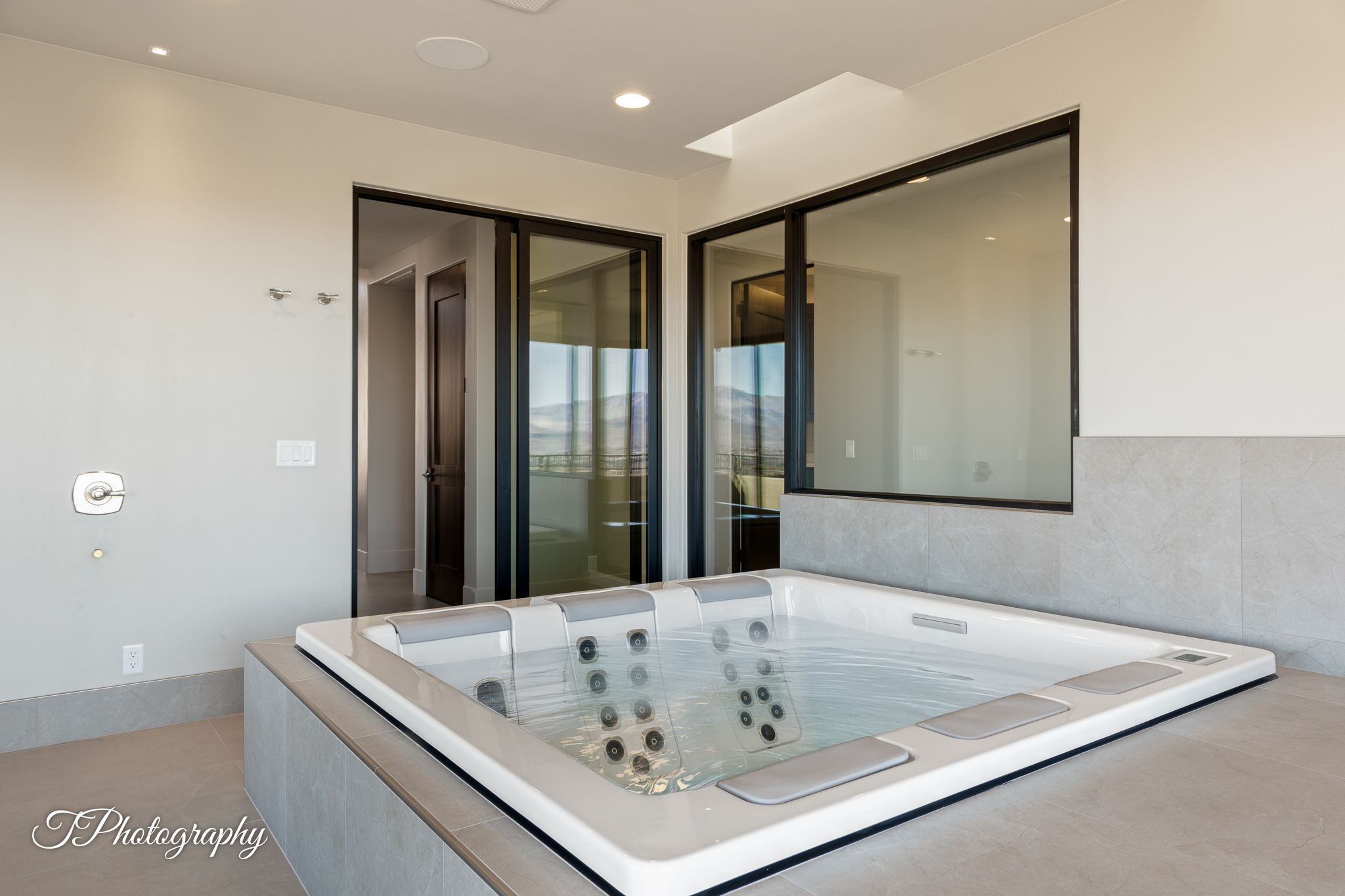 Built-in spa tub with surrounding light gray tiled platform, complemented by an overhead skylight and large fixed pane window