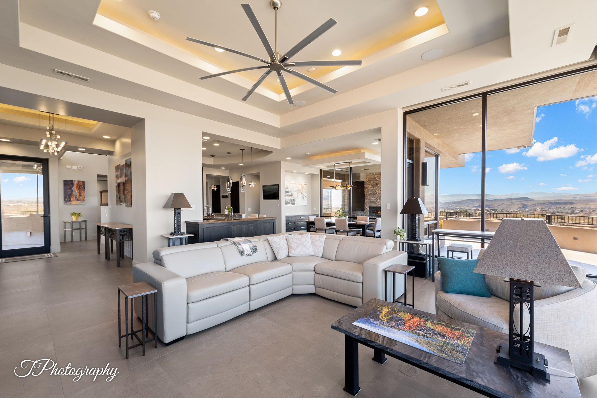 Spacious living area featuring floor-to-ceiling windows, tray ceilings with accent lighting, a large ceiling fan, and tile flooring
