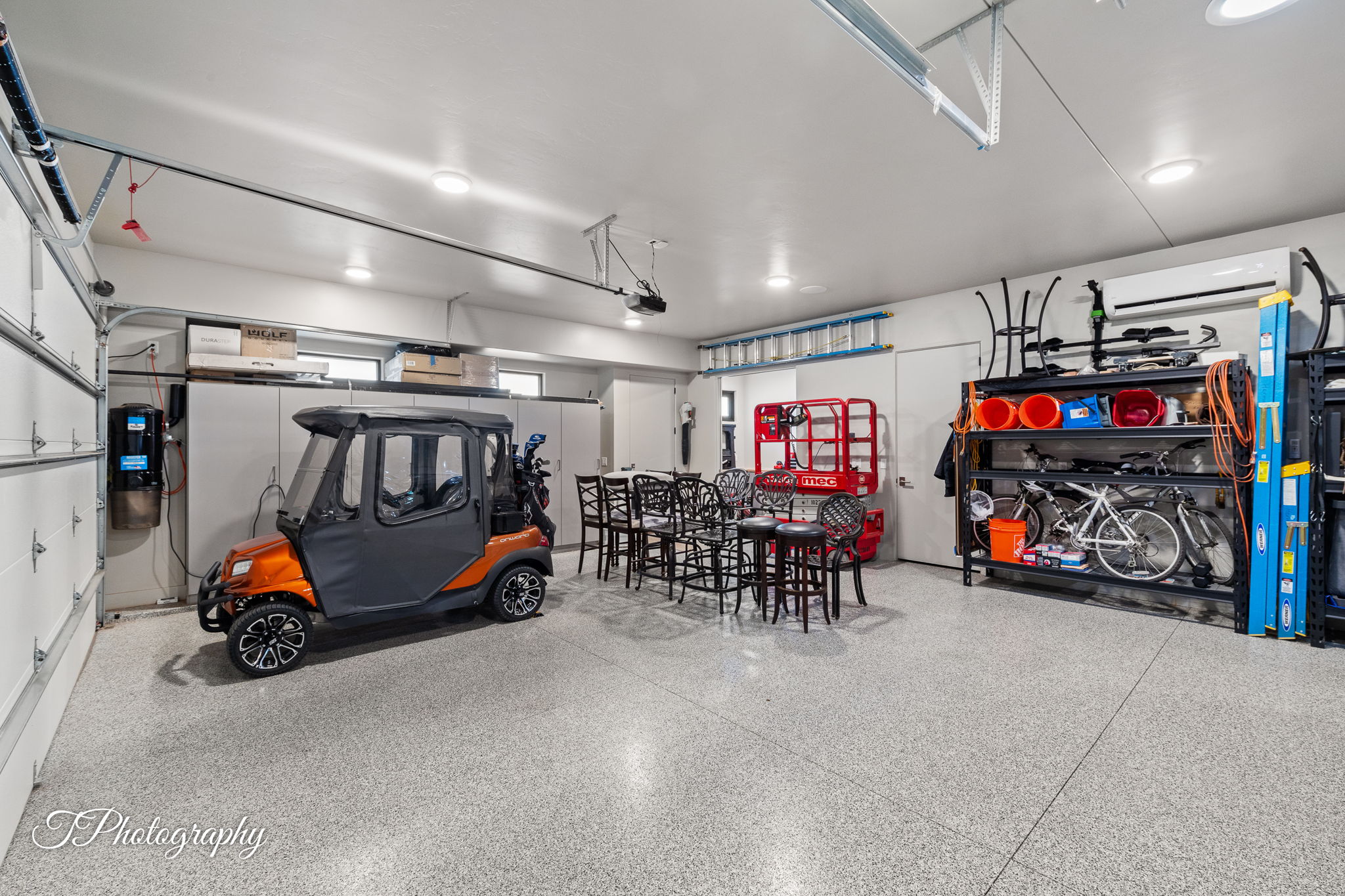 Spacious garage featuring a durable epoxy-coated floor, integrated ceiling lighting, and multiple storage solutions including built-in cabinetry and shelving units
