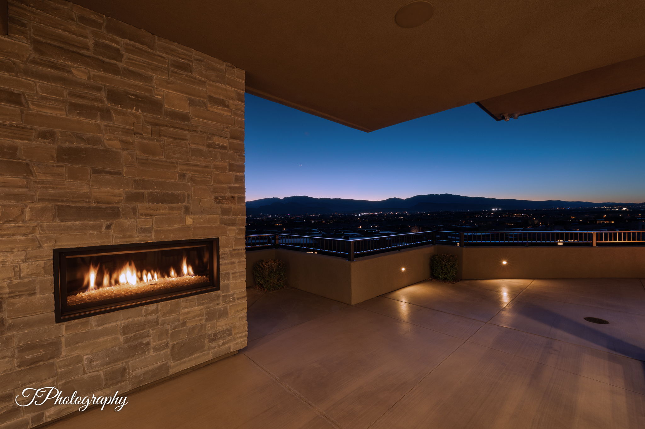 Expansive outdoor patio featuring a stone-clad fireplace with a linear firebox, integrated wall lighting, and a protective railing