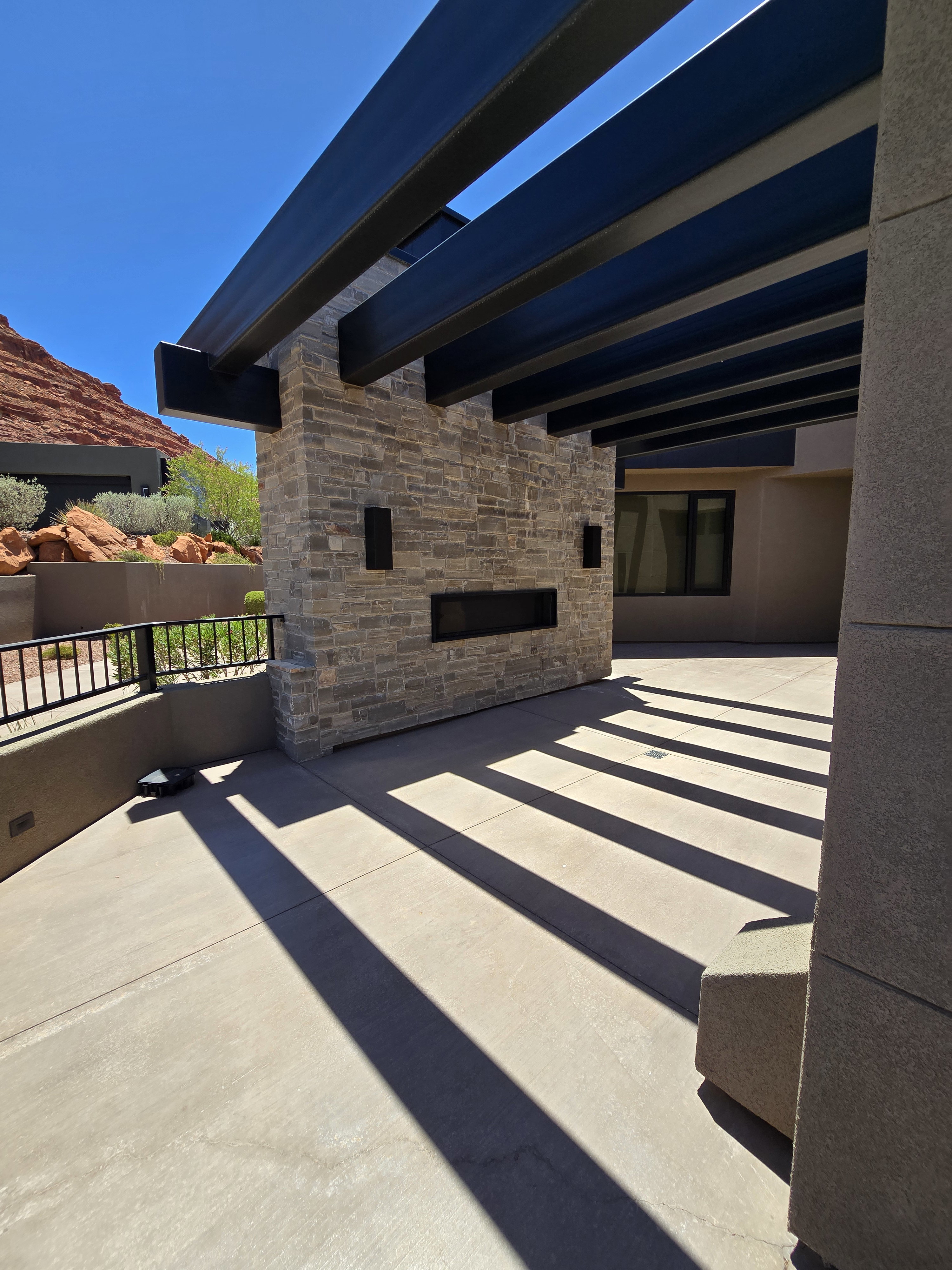 Outdoor living area featuring a stone-clad fireplace with a linear firebox, a pergola with dark beams, and a concrete patio