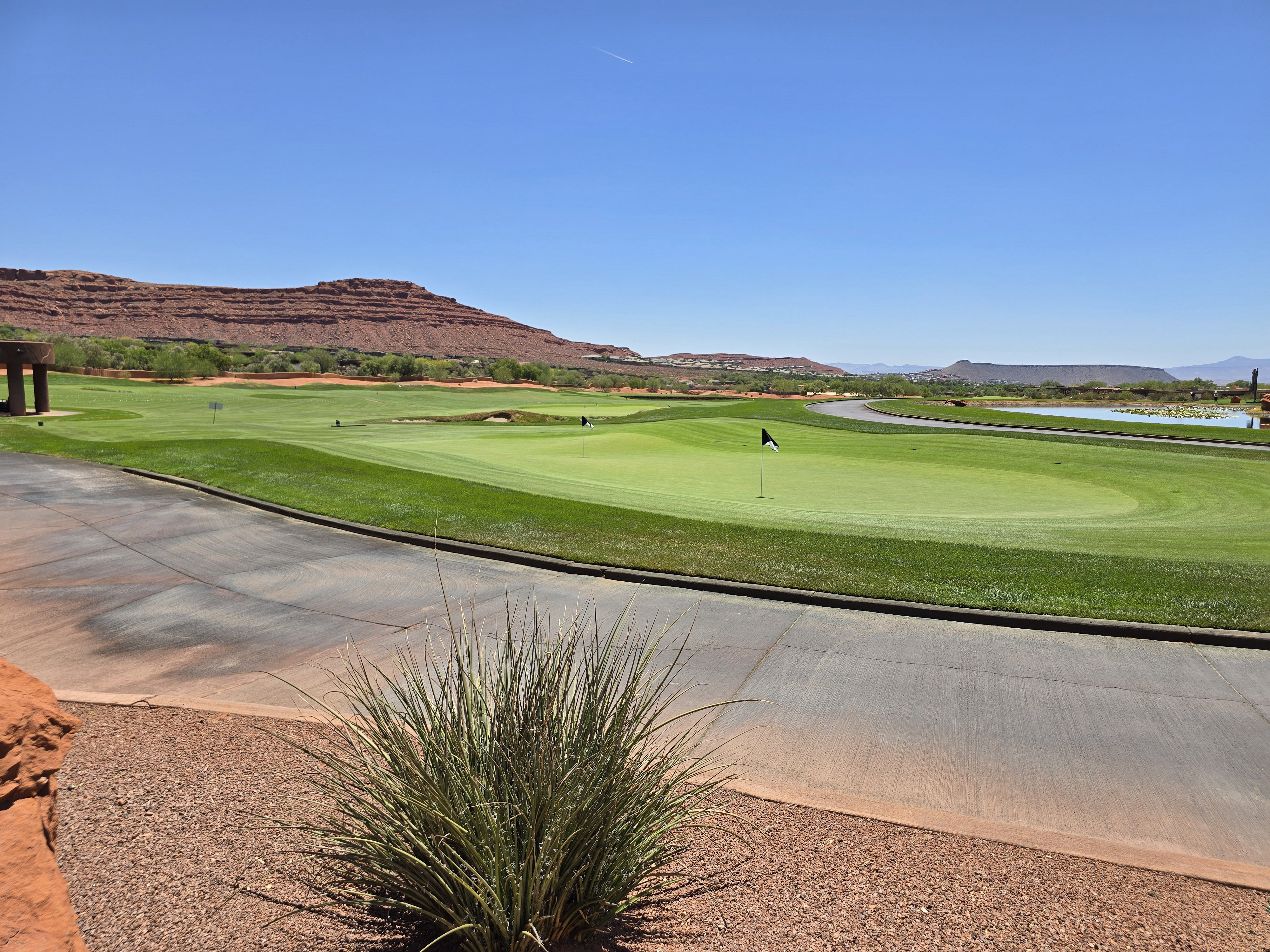 Golf course fairway and green with a flagstick, bordered by a paved cart path