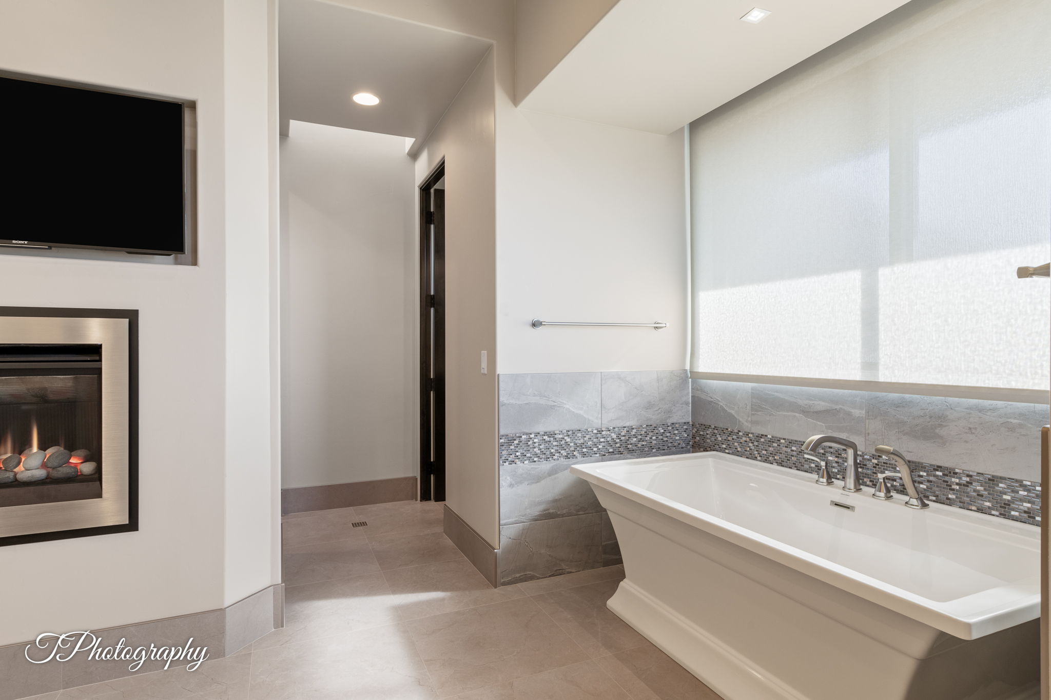 Freestanding soaking tub with chrome fixtures, set against a tiled accent wall with mosaic detailing