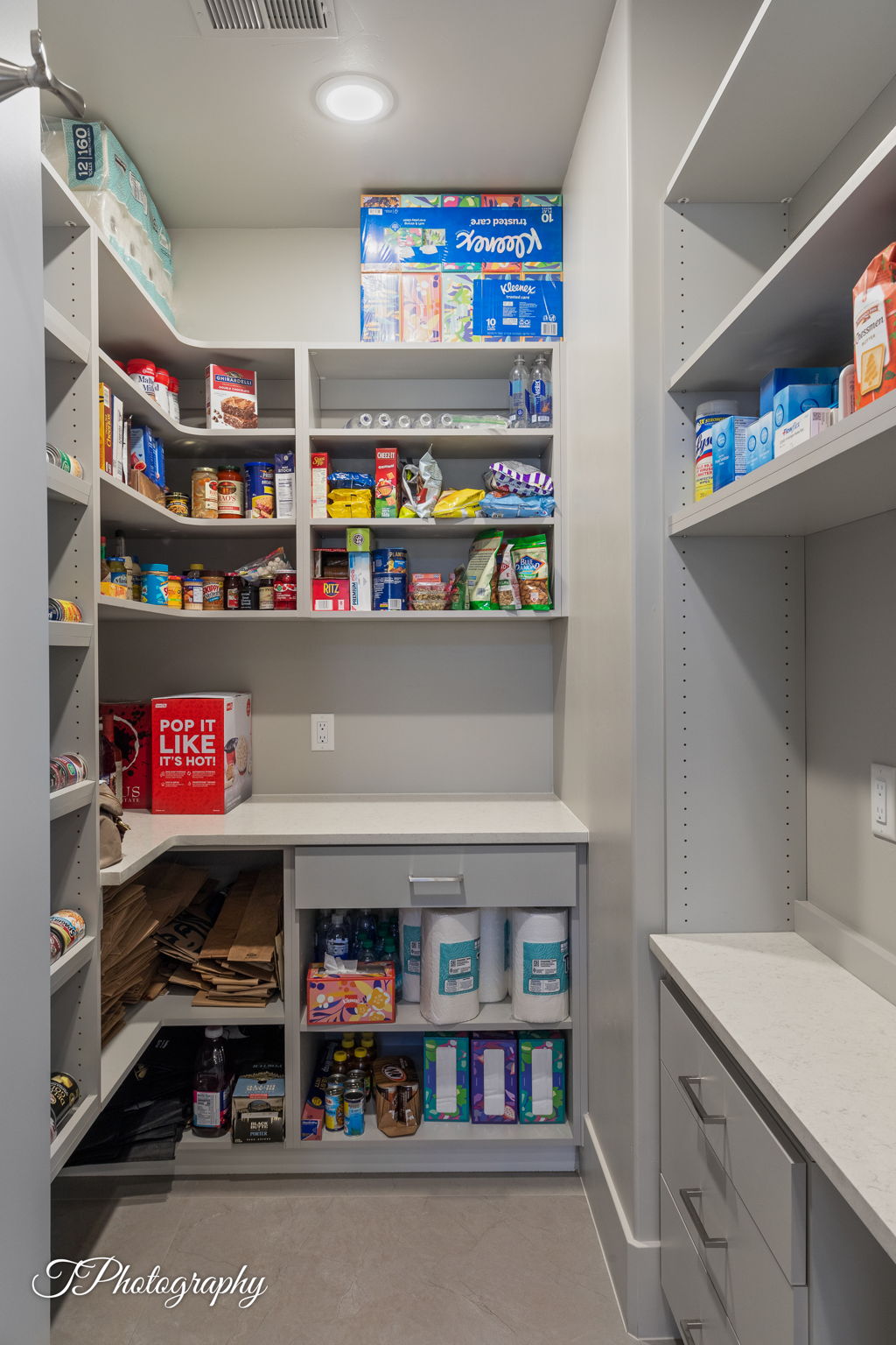 Walk-in pantry featuring custom built-in shelving, extensive countertop space, integrated cabinetry, recessed lighting, and durable flooring